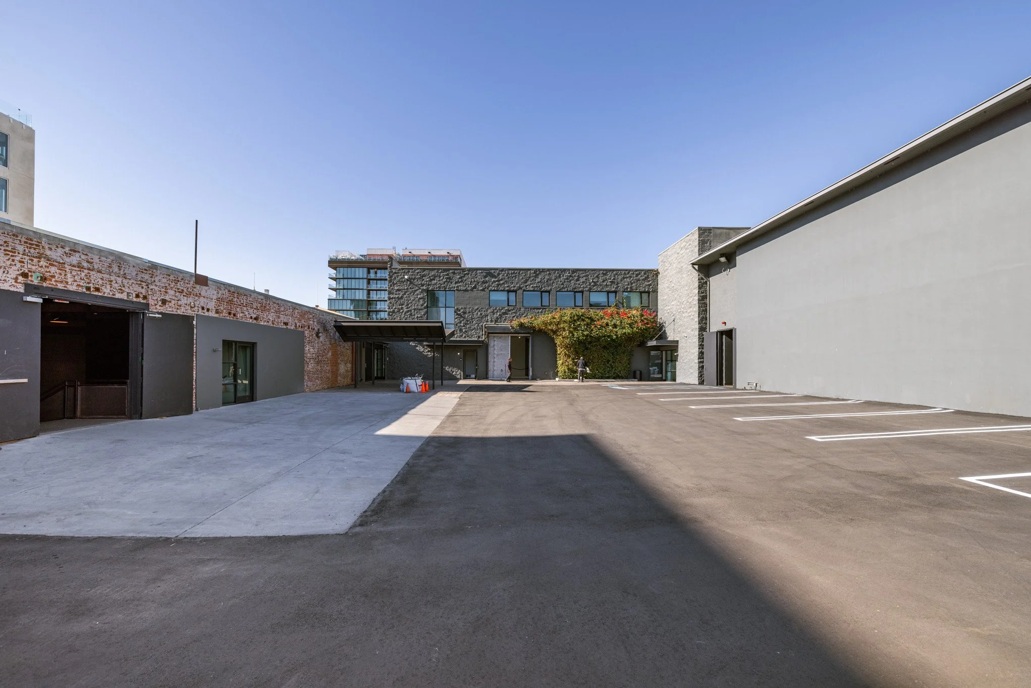 Empty parking lot adjacent to modern buildings with clear blue sky.