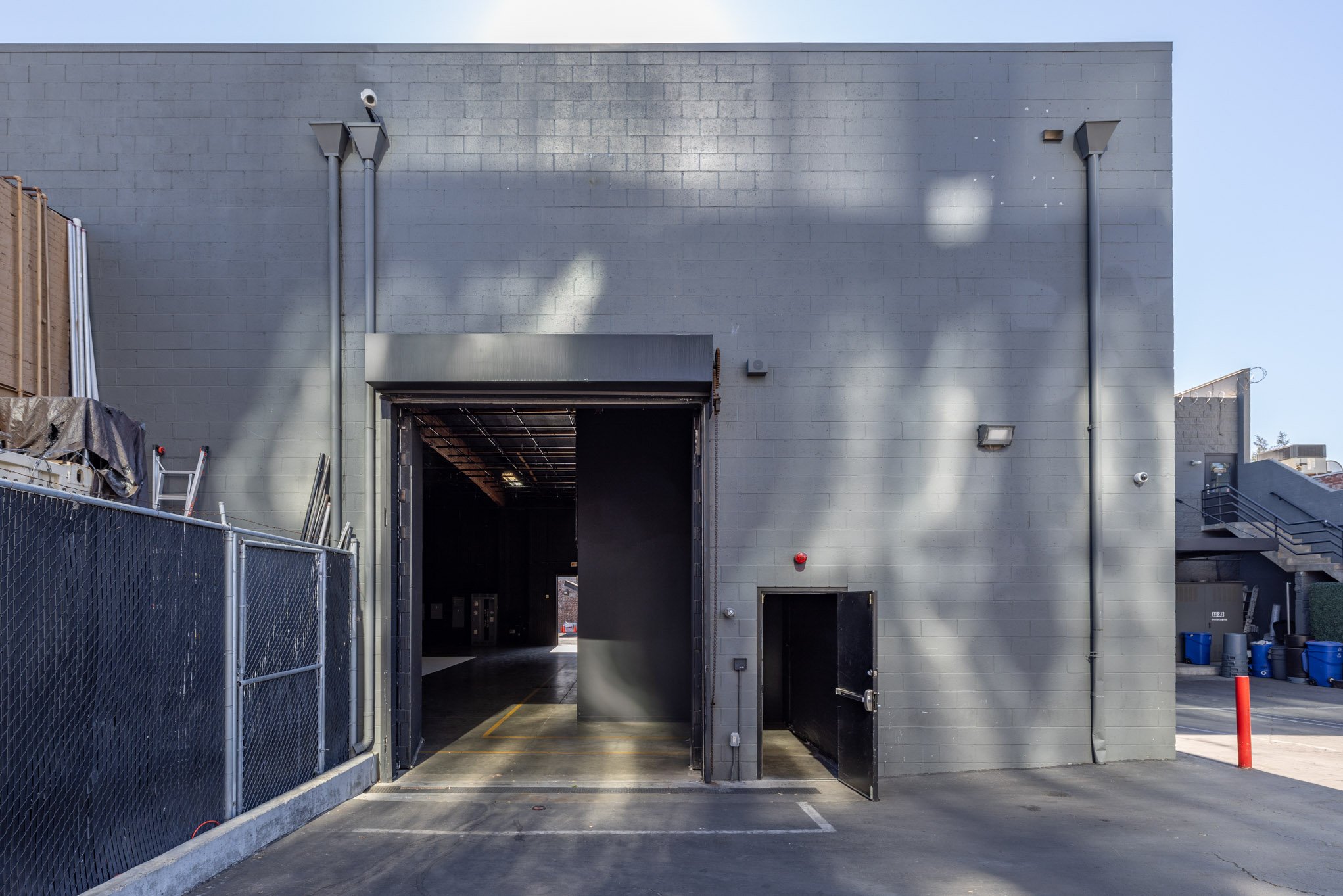 Back of a gray industrial building with a loading dock, small door, and outdoor lighting fixtures.
