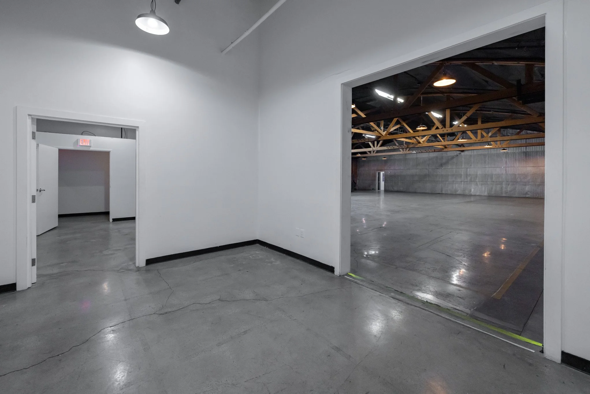 Empty industrial interior with white walls, polished concrete floors, large open space, and visible ceiling beams.