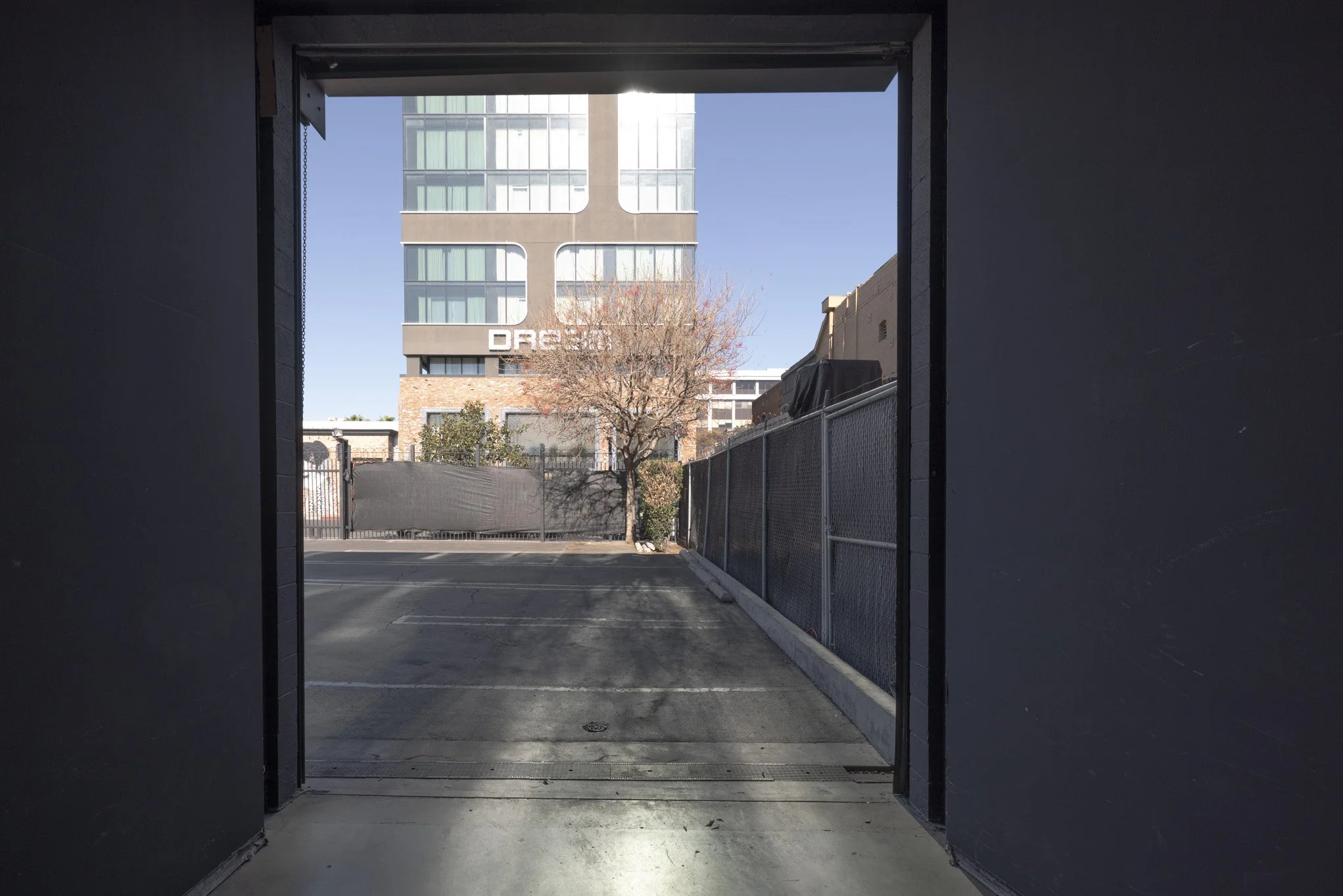 View of an outdoor parking lot seen through a tunnel entrance, with a tree and a modern building in the background.