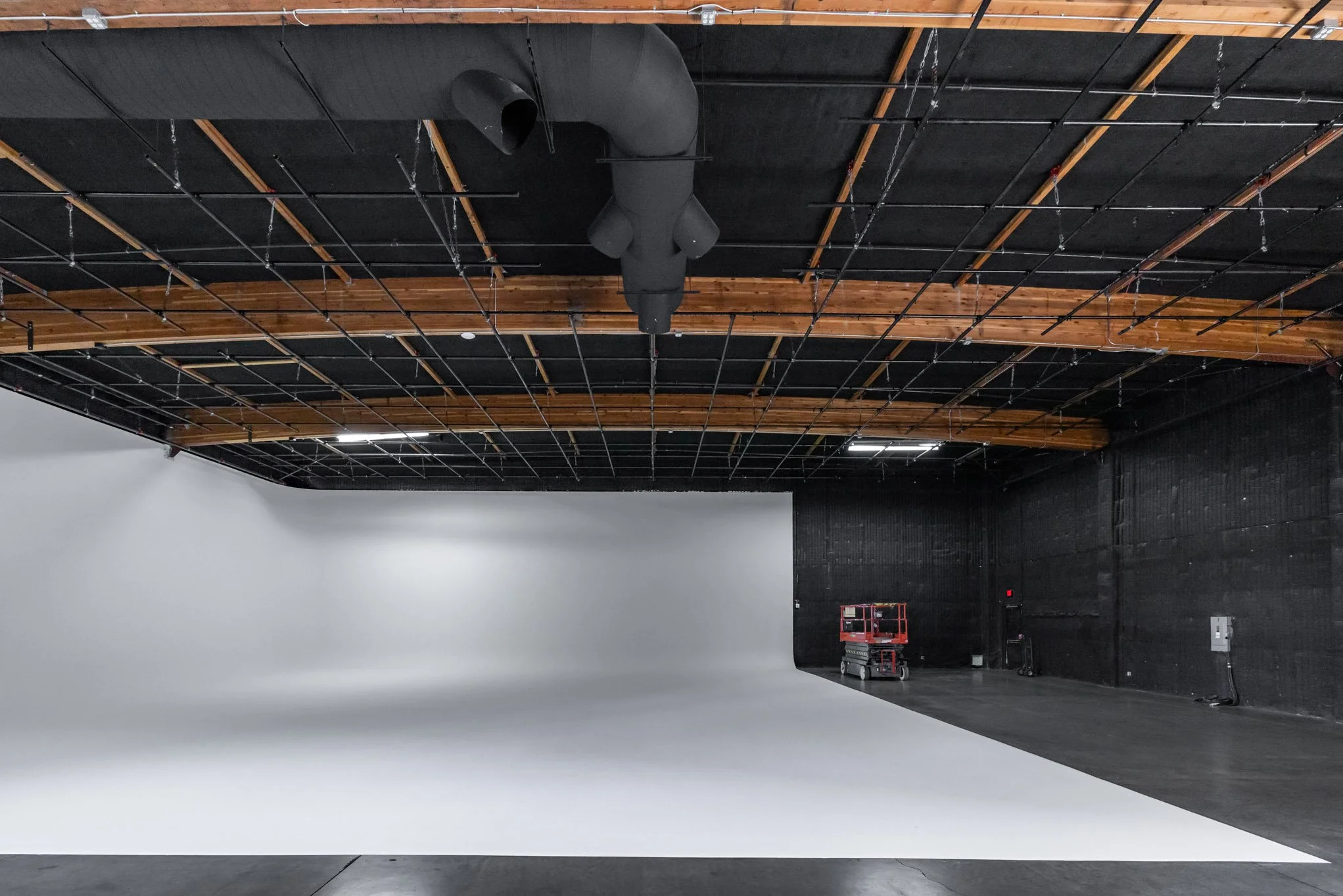 Large photography studio with a white curved backdrop, black walls, wooden ceiling accents, and overhead lighting