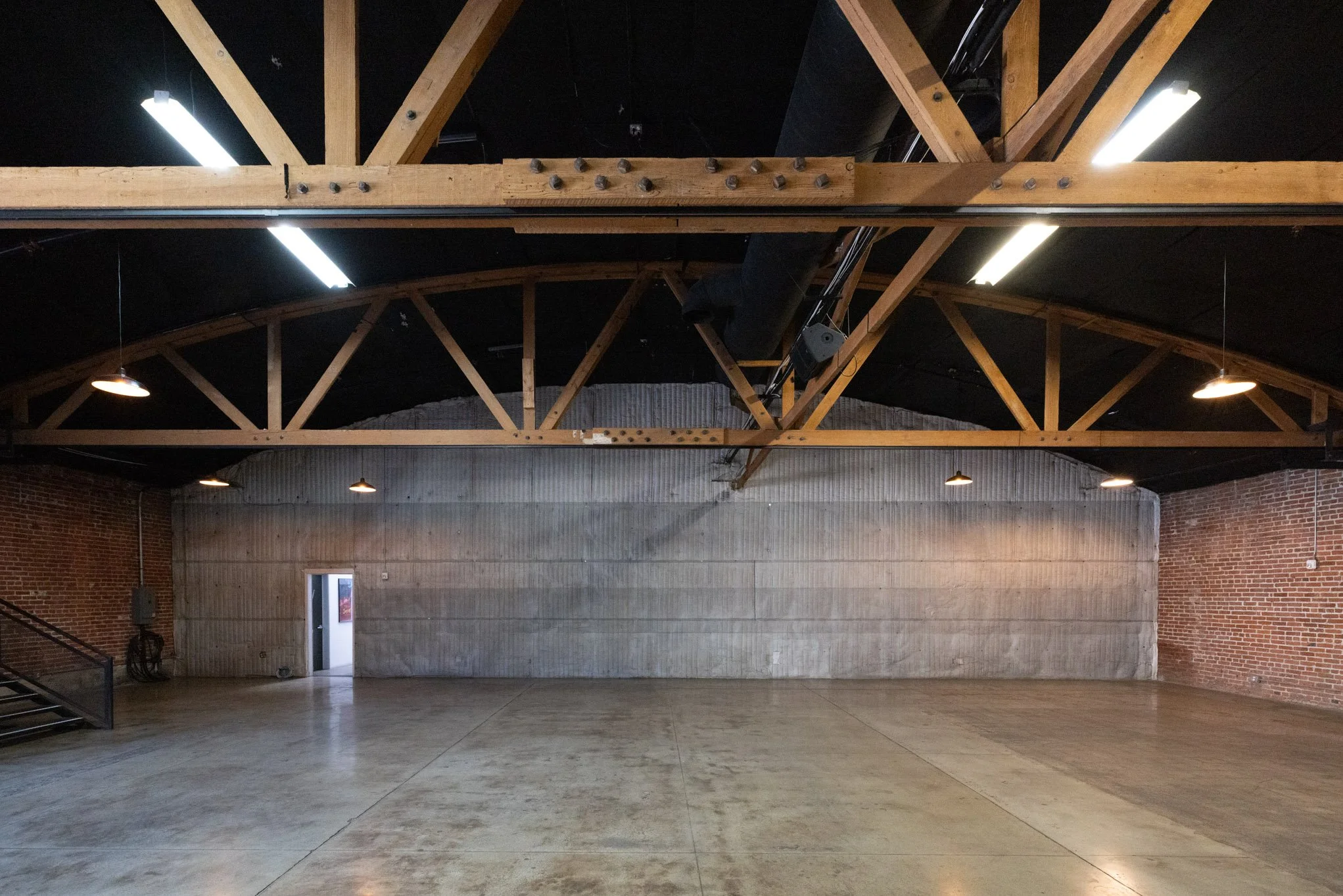Empty industrial-style room with concrete walls, brick walls on sides, wooden ceiling beams, and polished concrete floor.