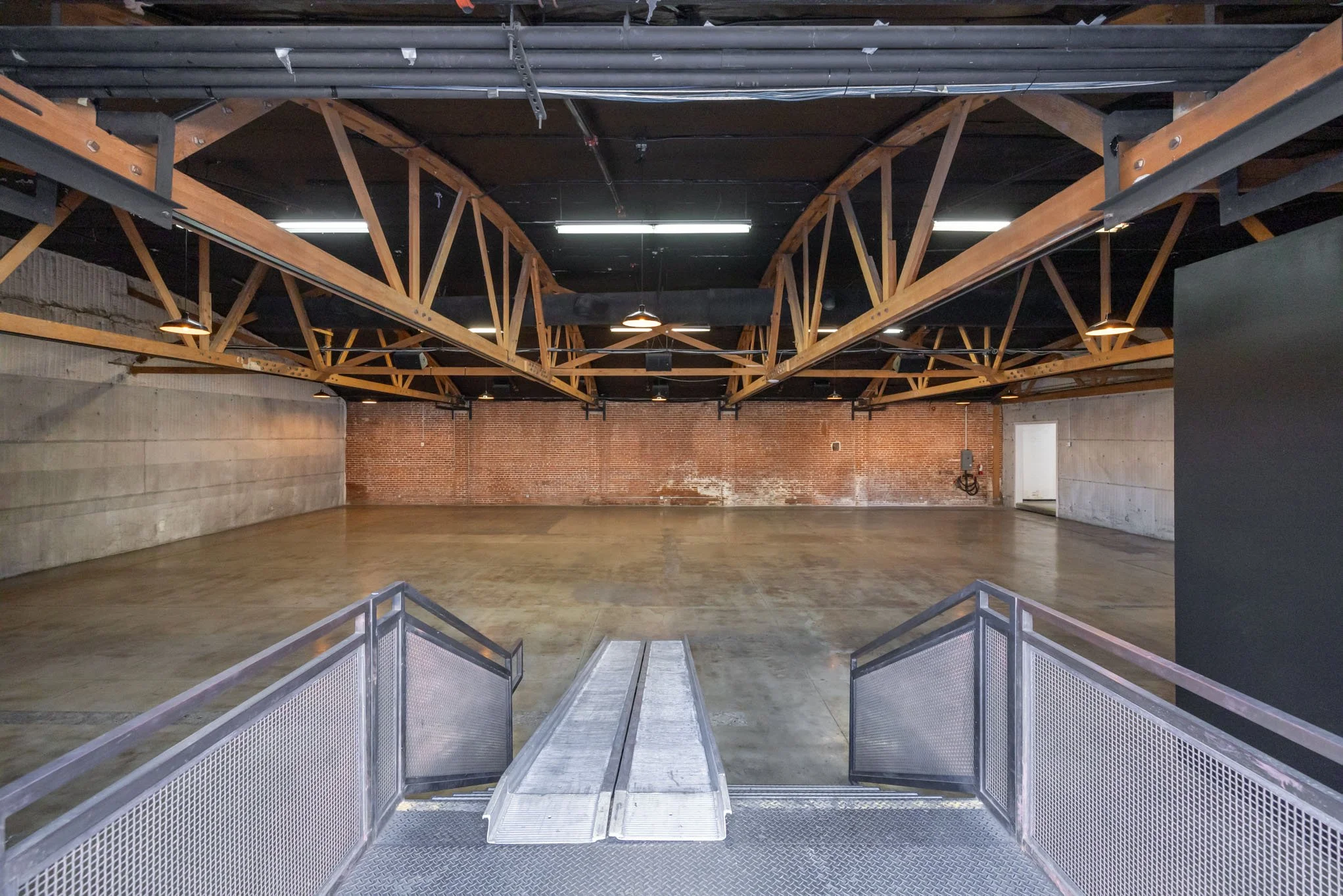 Empty indoor space with concrete walls, wooden ceiling beams, and a metal ramp.