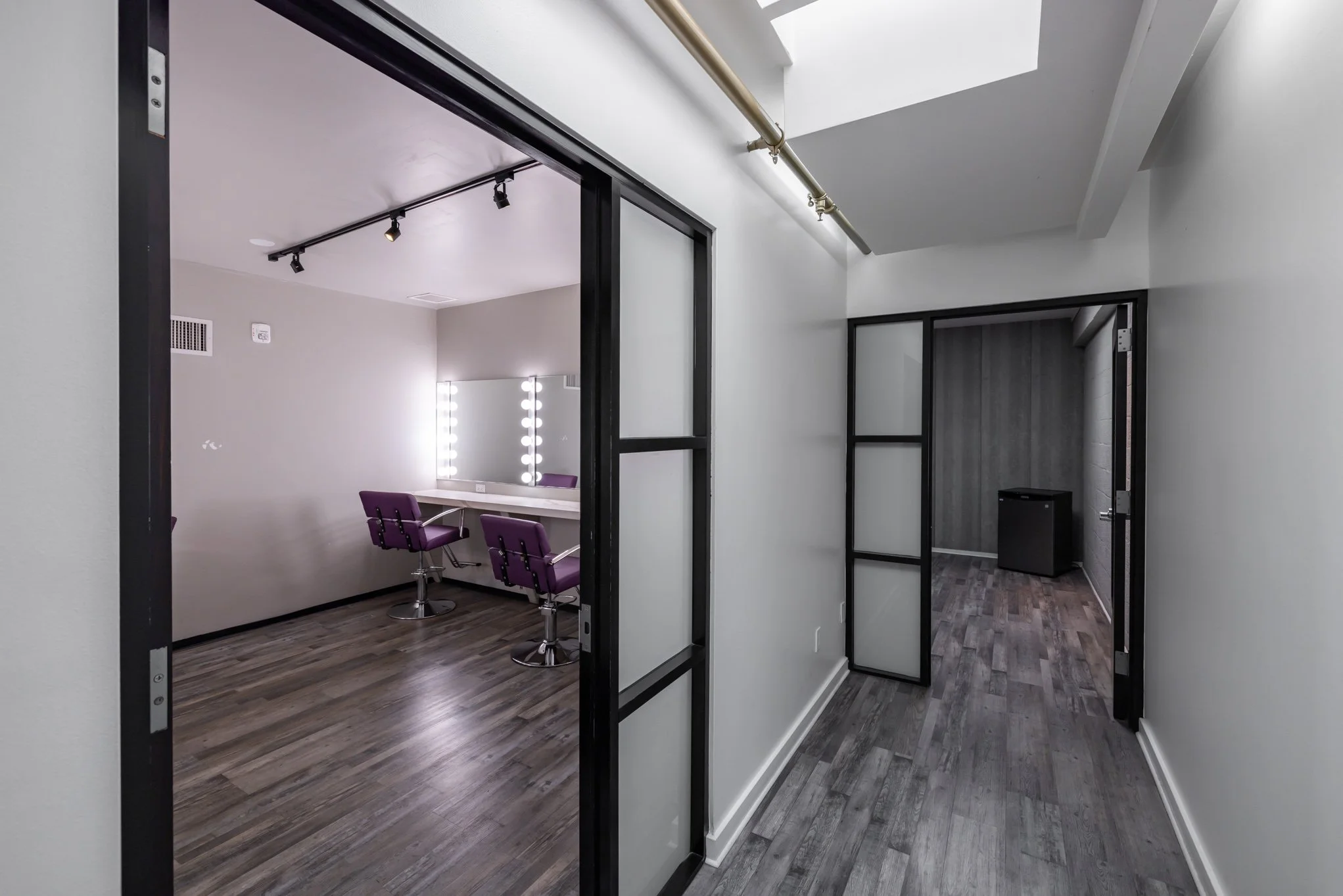 Empty hallway leading to a dressing room with purple chairs and a mirror with lights