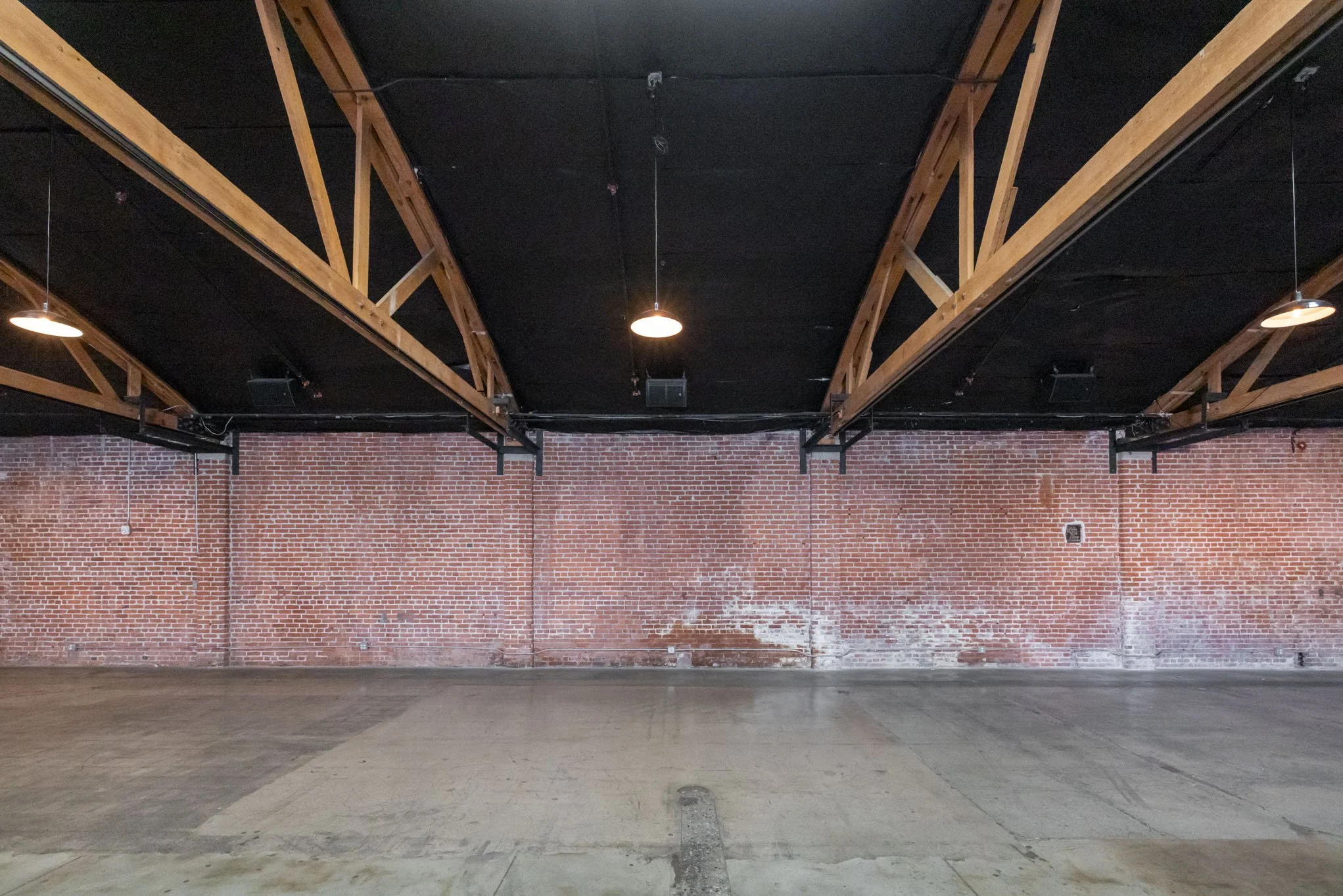 Empty industrial-style room with brick wall, exposed wooden beams, and ceiling lights.