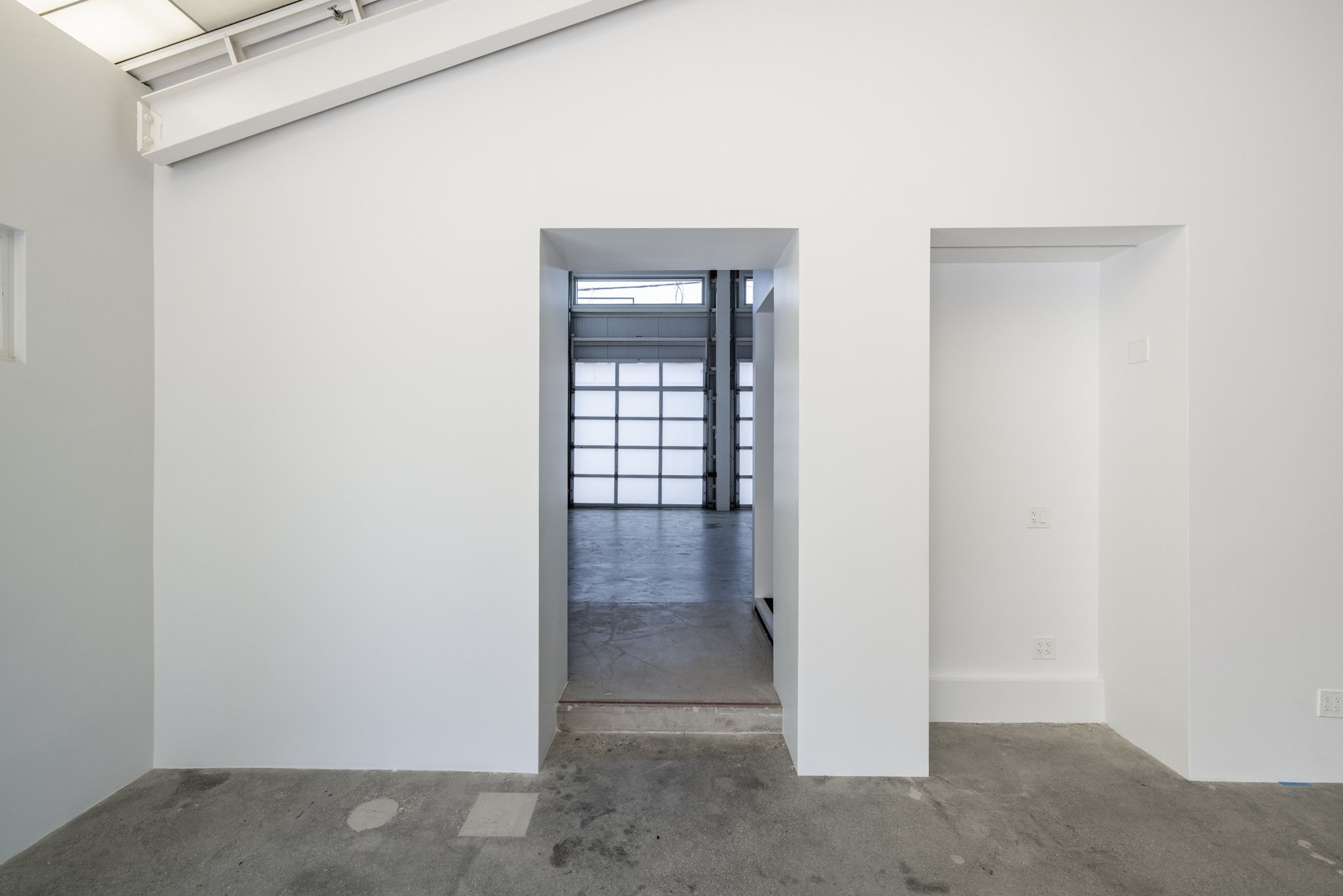 Empty white room with concrete floor leading to a garage with a transparent garage door.