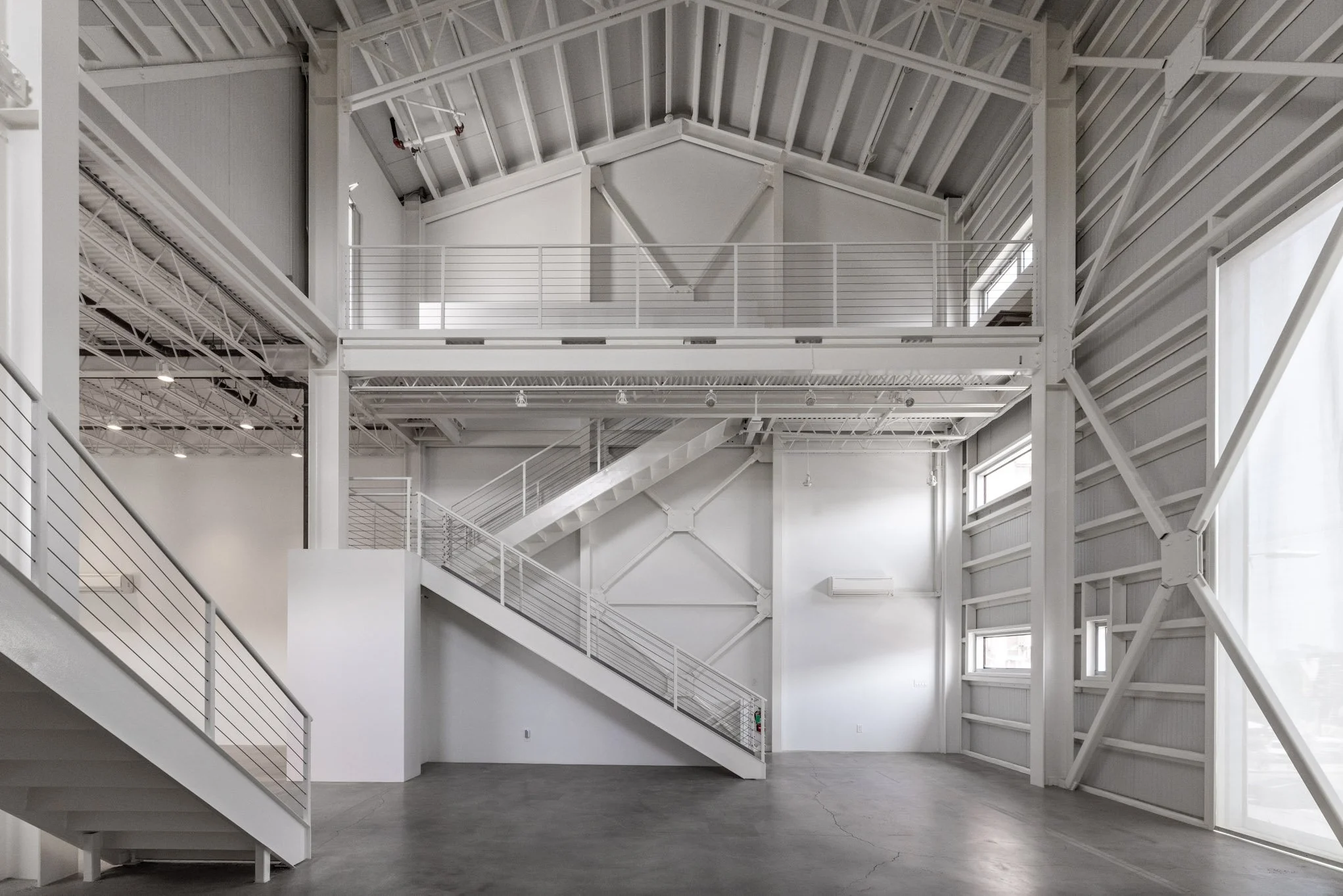 Interior of a modern industrial building with white walls, exposed structural elements, metal staircase and walkways, large windows, and high ceiling.
