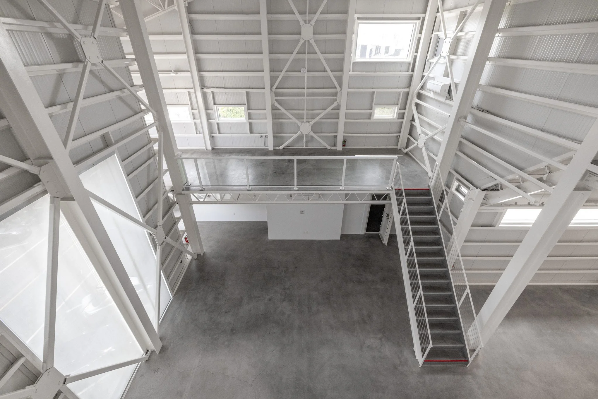 Interior view of a white industrial-style building with metal framework, concrete floor, and stairs leading to an upper level.