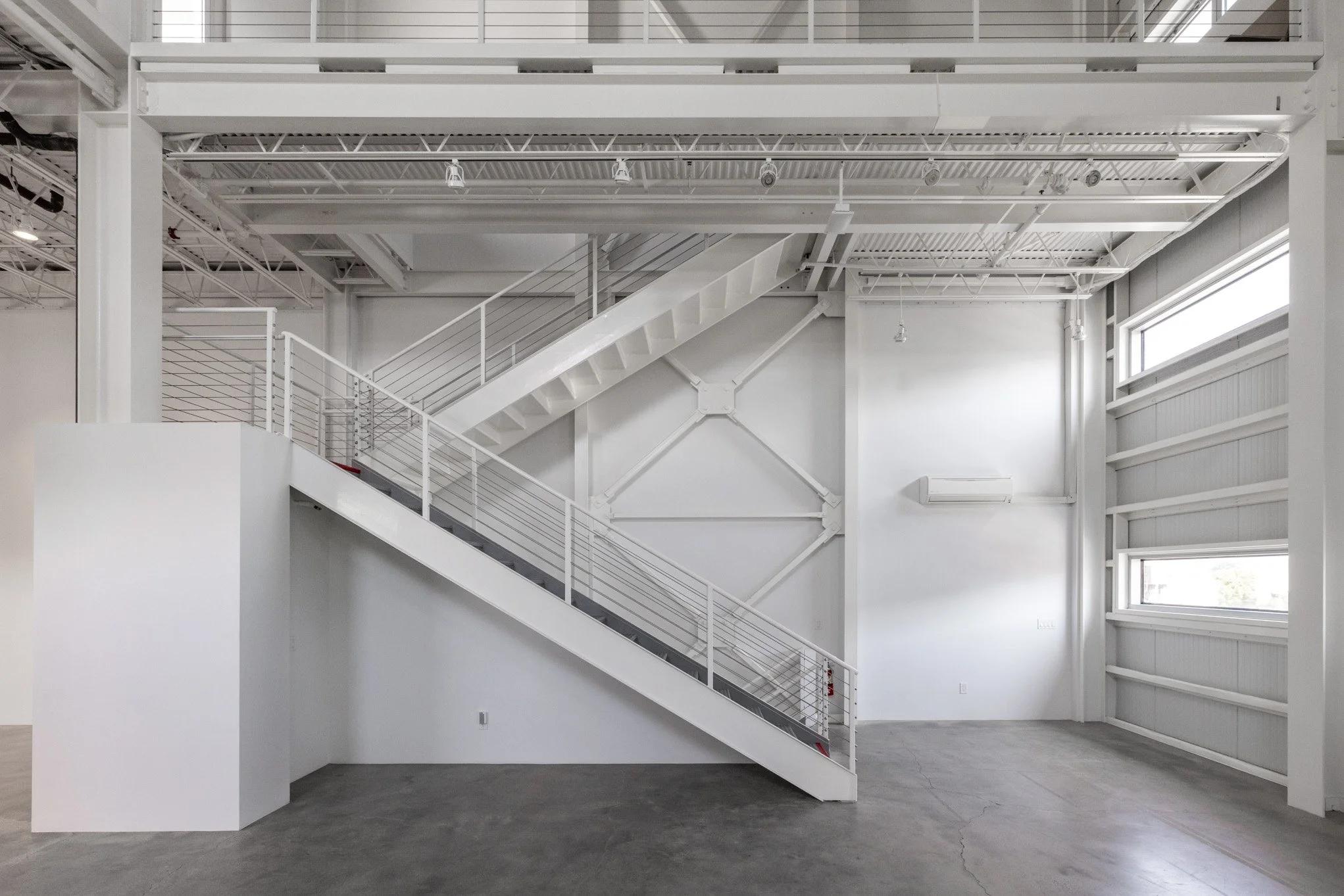Empty modern industrial interior with white walls, metal staircase, high ceiling, and windows.