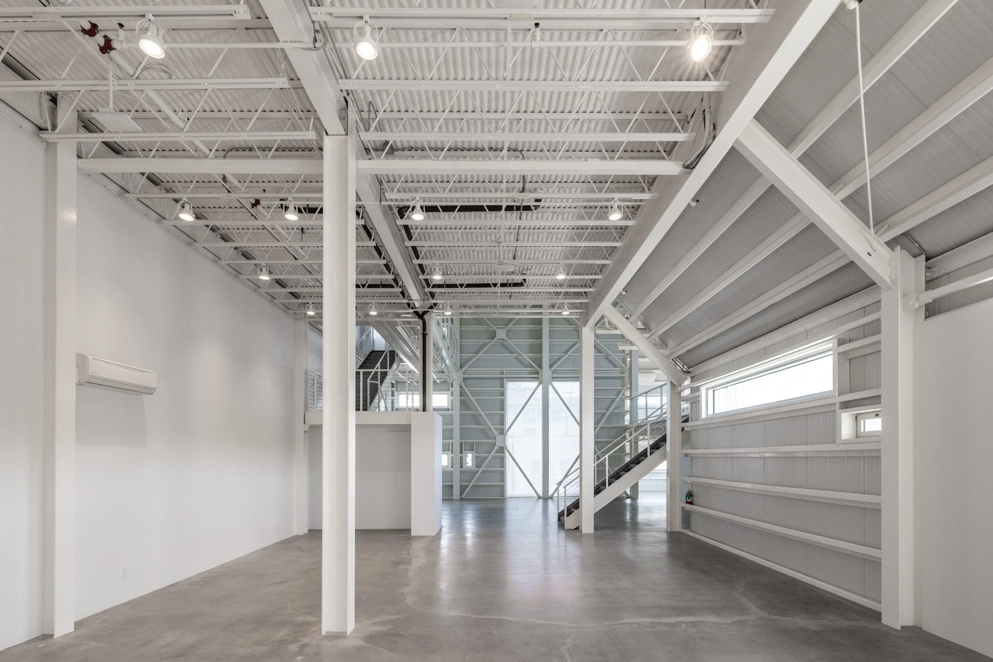 Empty interior space with white walls and ceiling, concrete floor, and metal staircase with railing.
