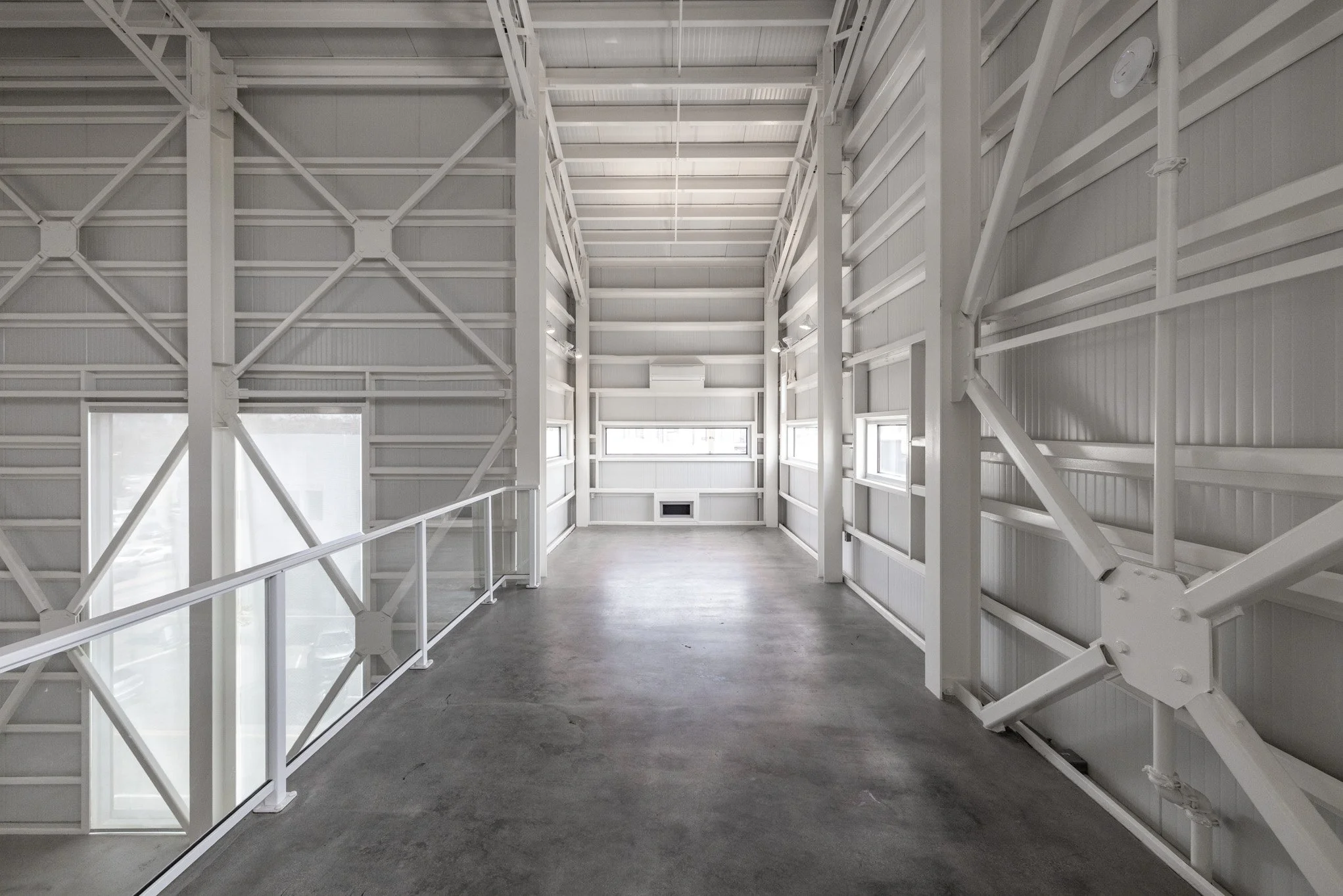 Empty white industrial-style balcony with metal railings and windows, concrete floor, and steel beams.