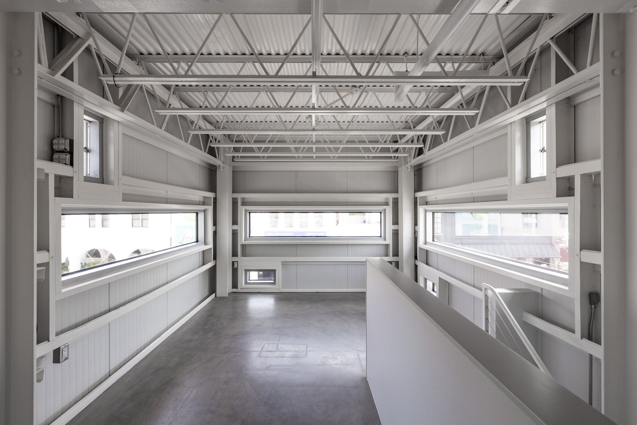 Interior view of a modern building with white walls, high ceiling with exposed beams, and horizontal windows letting in natural light.