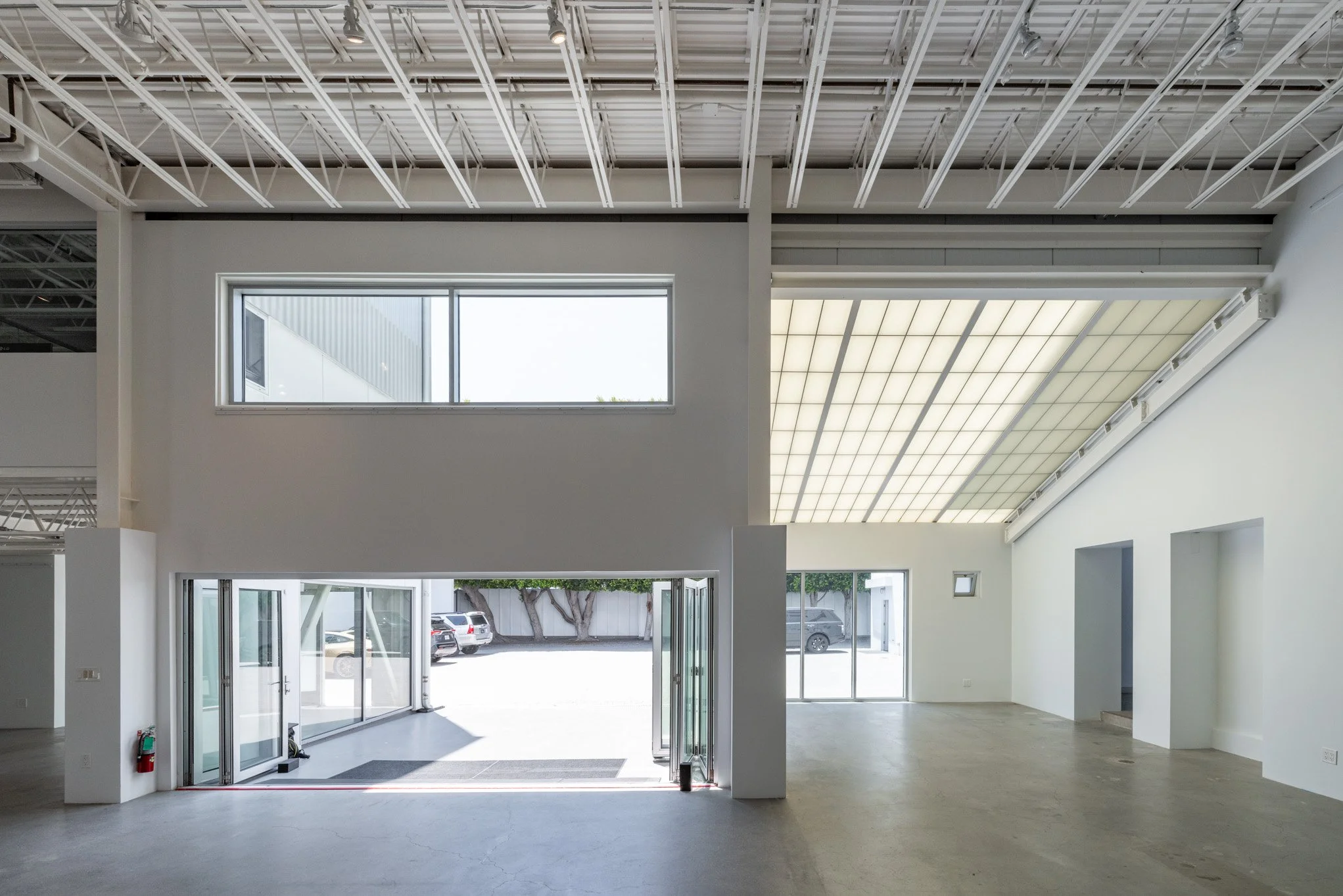Empty commercial space with white walls, large windows, open floor plan, concrete floor, and skylight ceiling.
