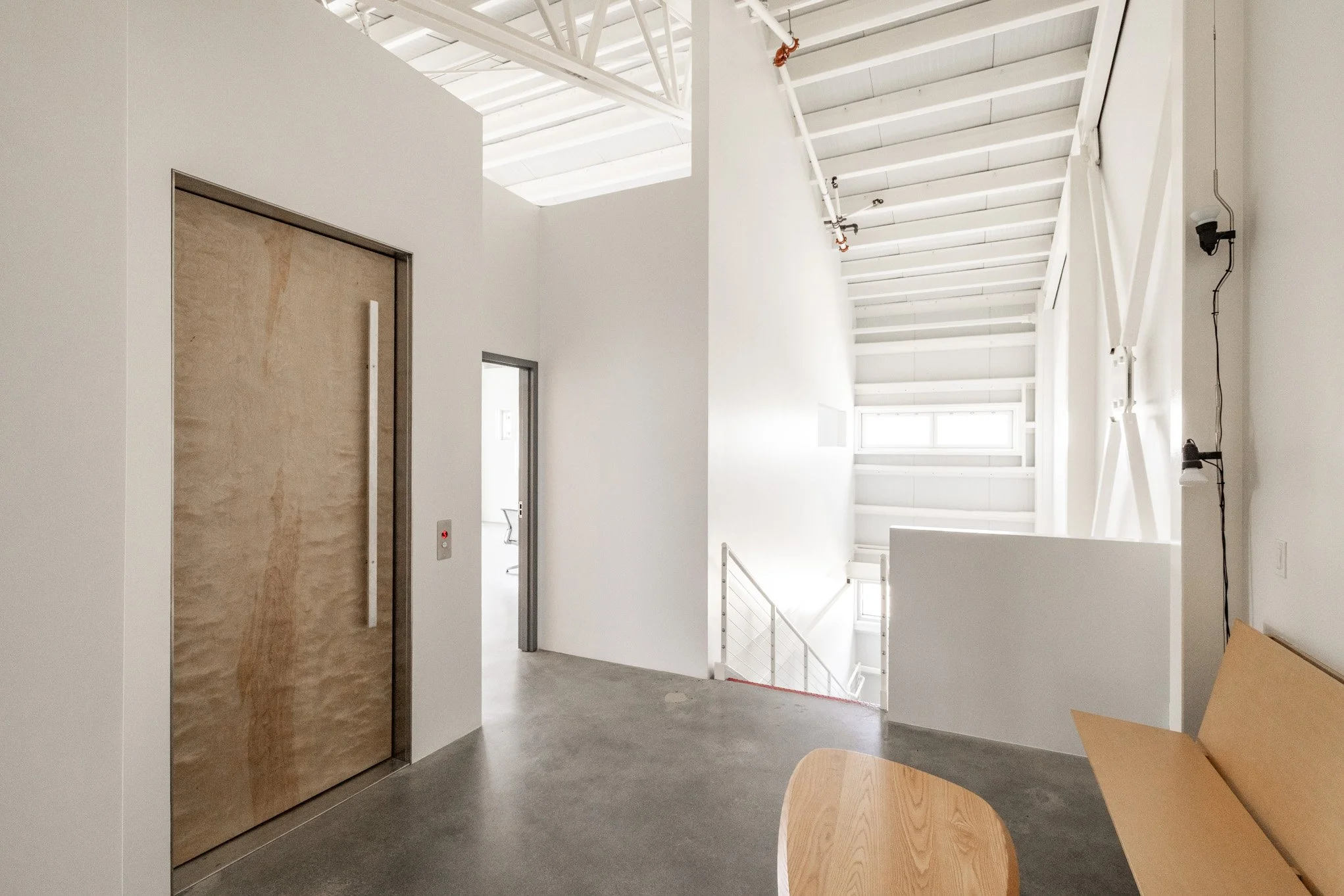 Modern interior space with an elevator, a doorway, a staircase, and natural light from windows.