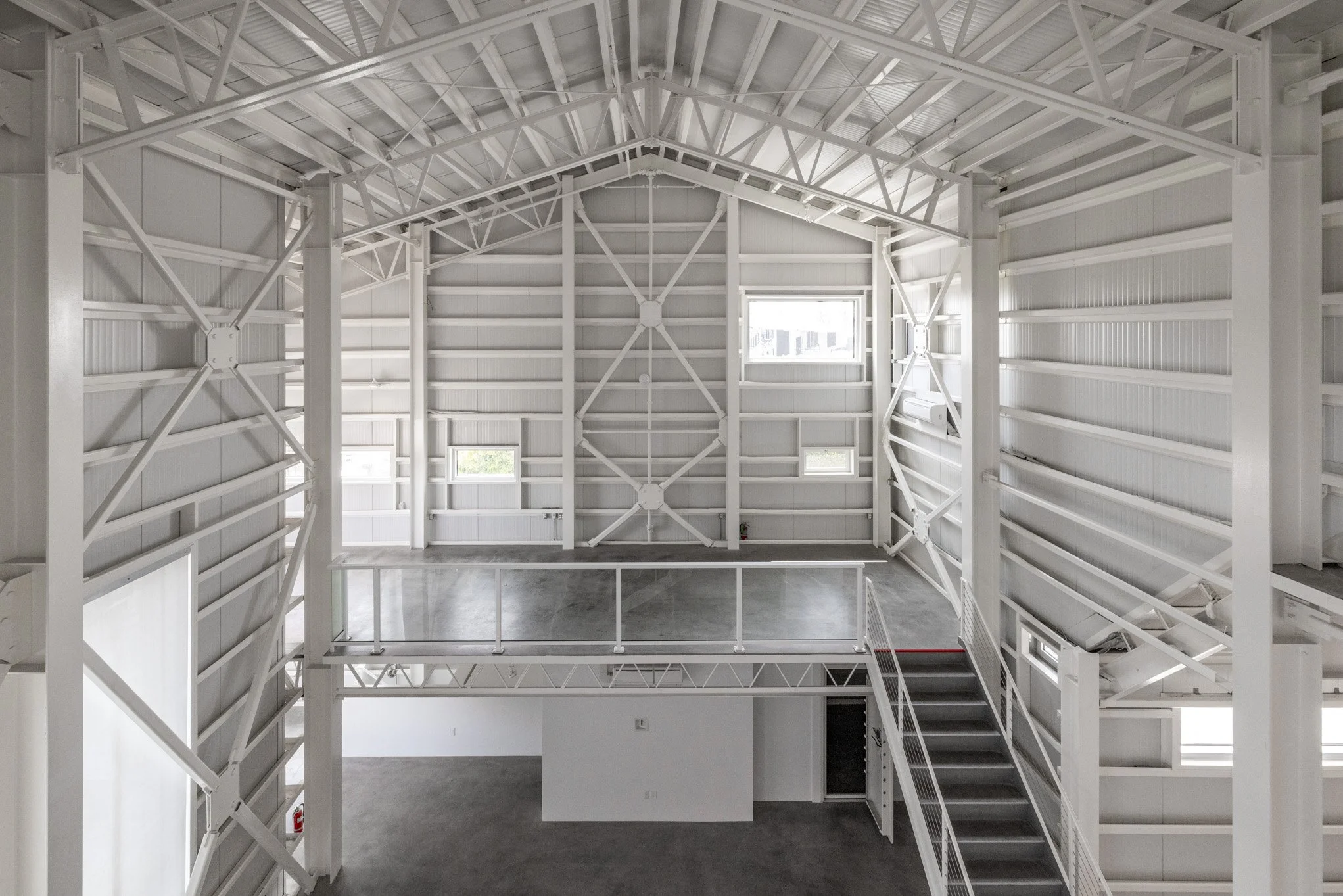 Interior view of an industrial-style building with white steel framing, high vaulted ceiling, and multiple windows allowing natural light.