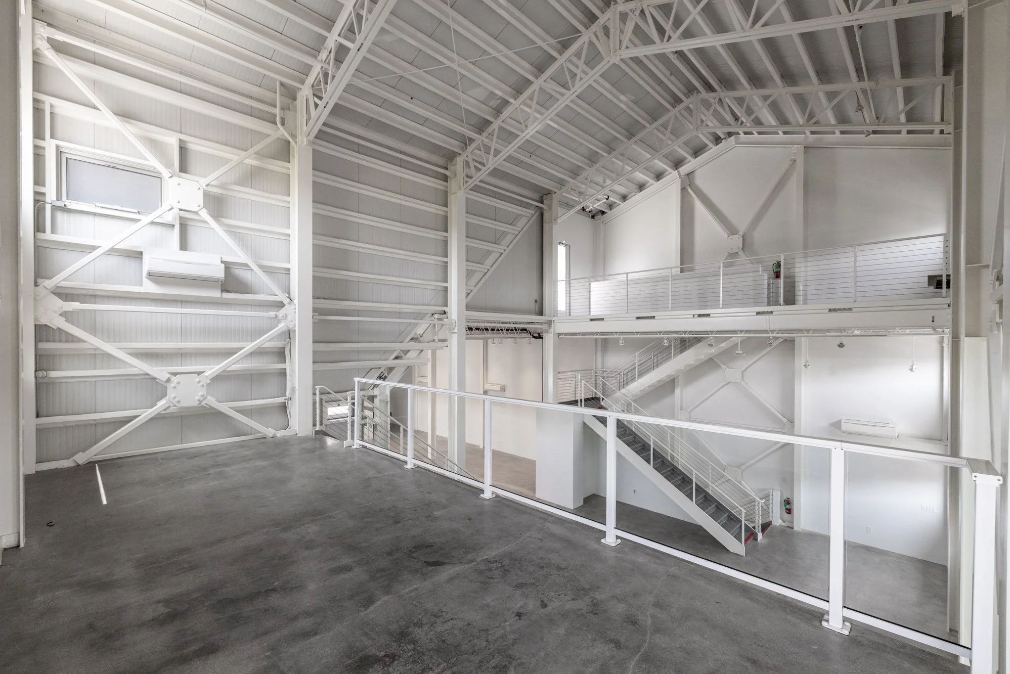 Empty, modern industrial interior with white metal beams, stairs, and rails, concrete floor, and high ceiling.
