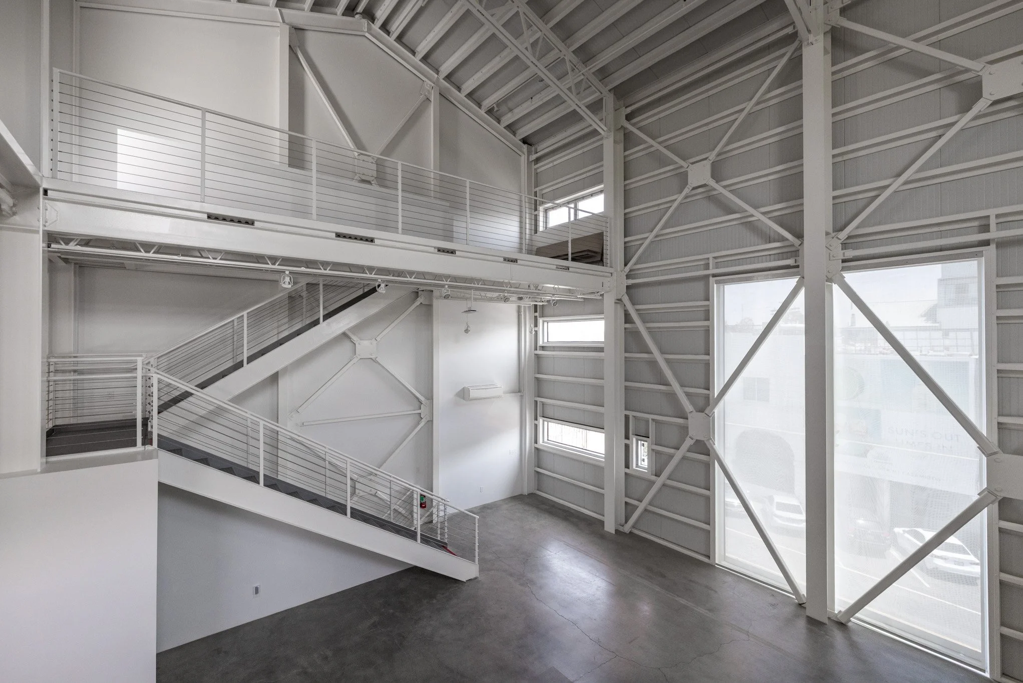 Interior of a modern, empty multi-level industrial or commercial building with metal staircases, white walls, large windows, and exposed structural beams.
