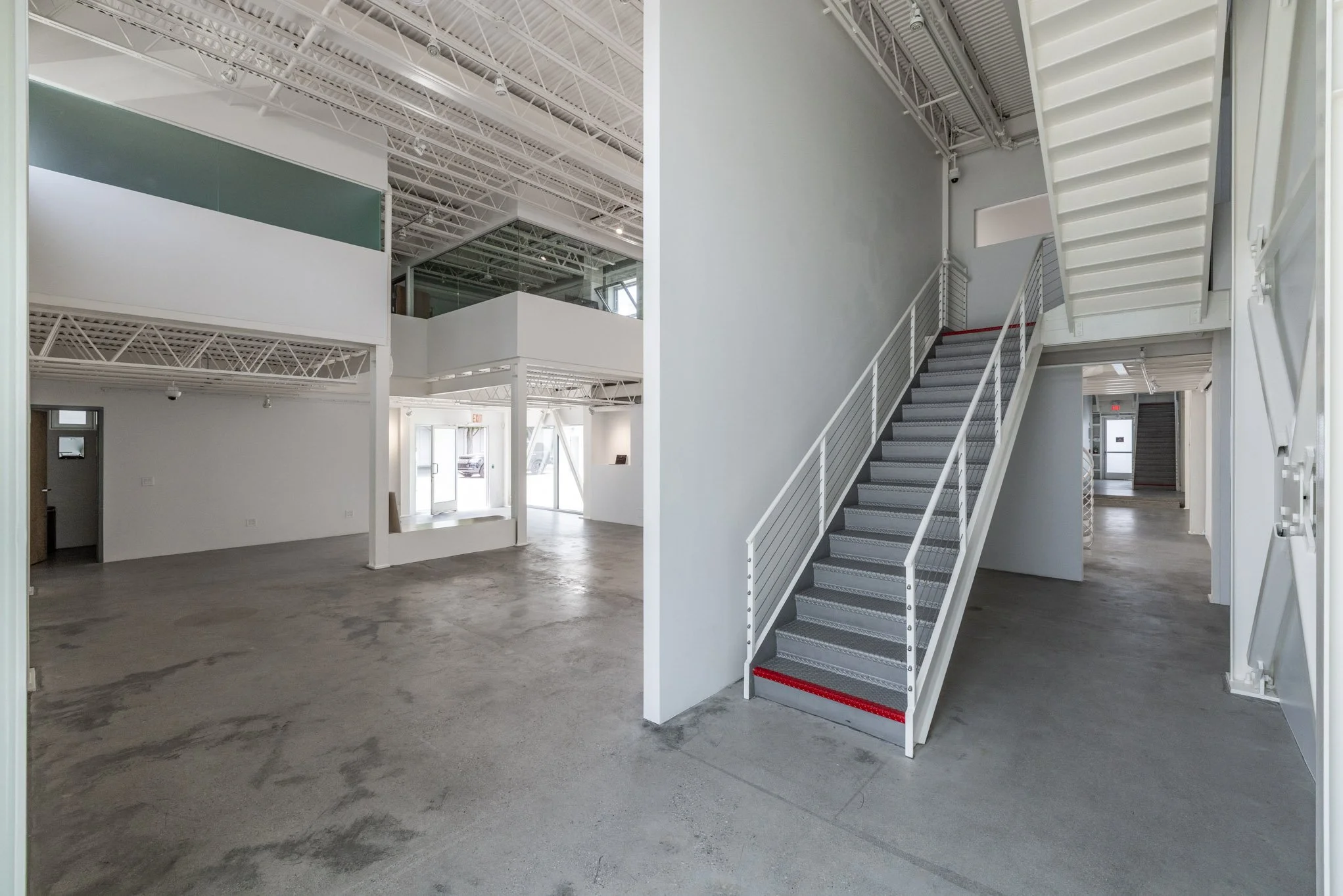 Empty commercial space with concrete floor, white walls, metal staircase, and modern interior design.