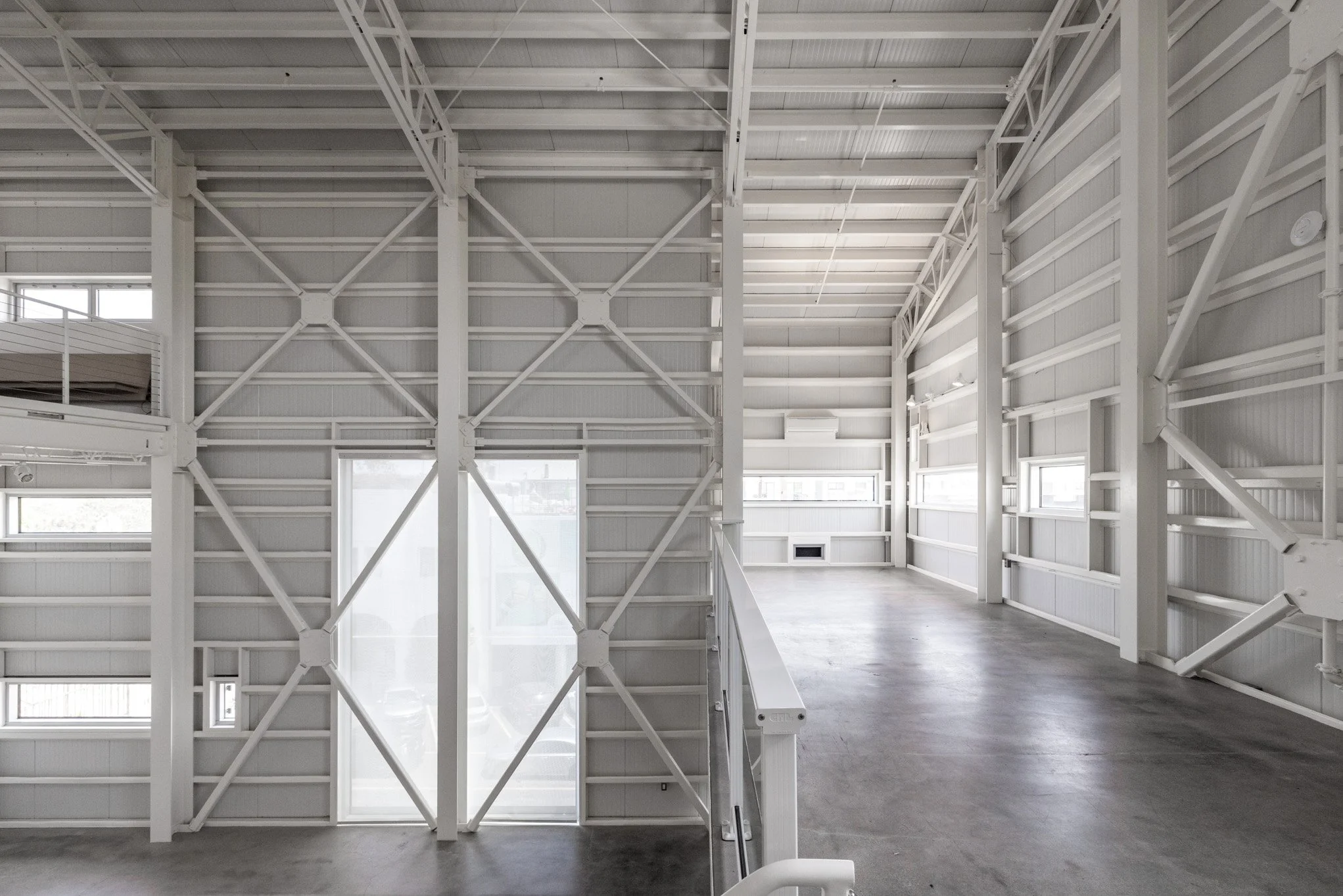 Spacious industrial loft with white steel beams, high ceiling, multiple windows, and polished concrete floor.