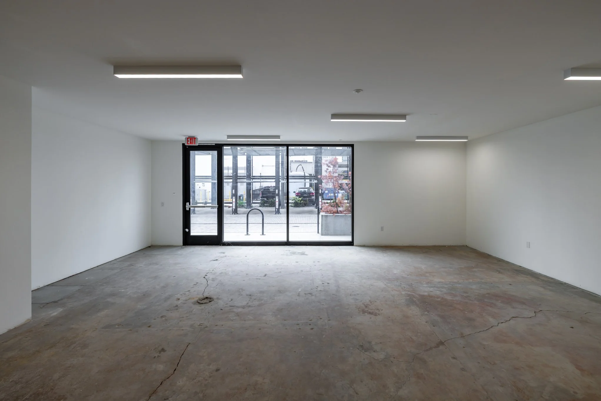 Empty commercial space with white walls, concrete floor, and glass entrance doors with outdoor view.