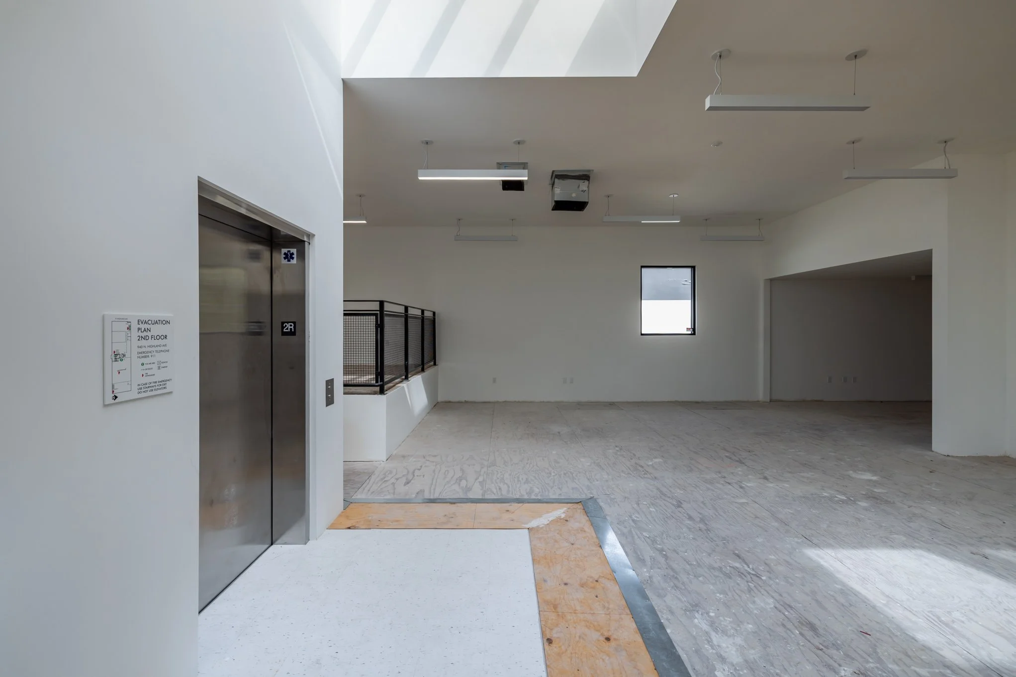 Empty indoor space with white walls, a window, and an elevator with a sign next to it, under construction or renovation.