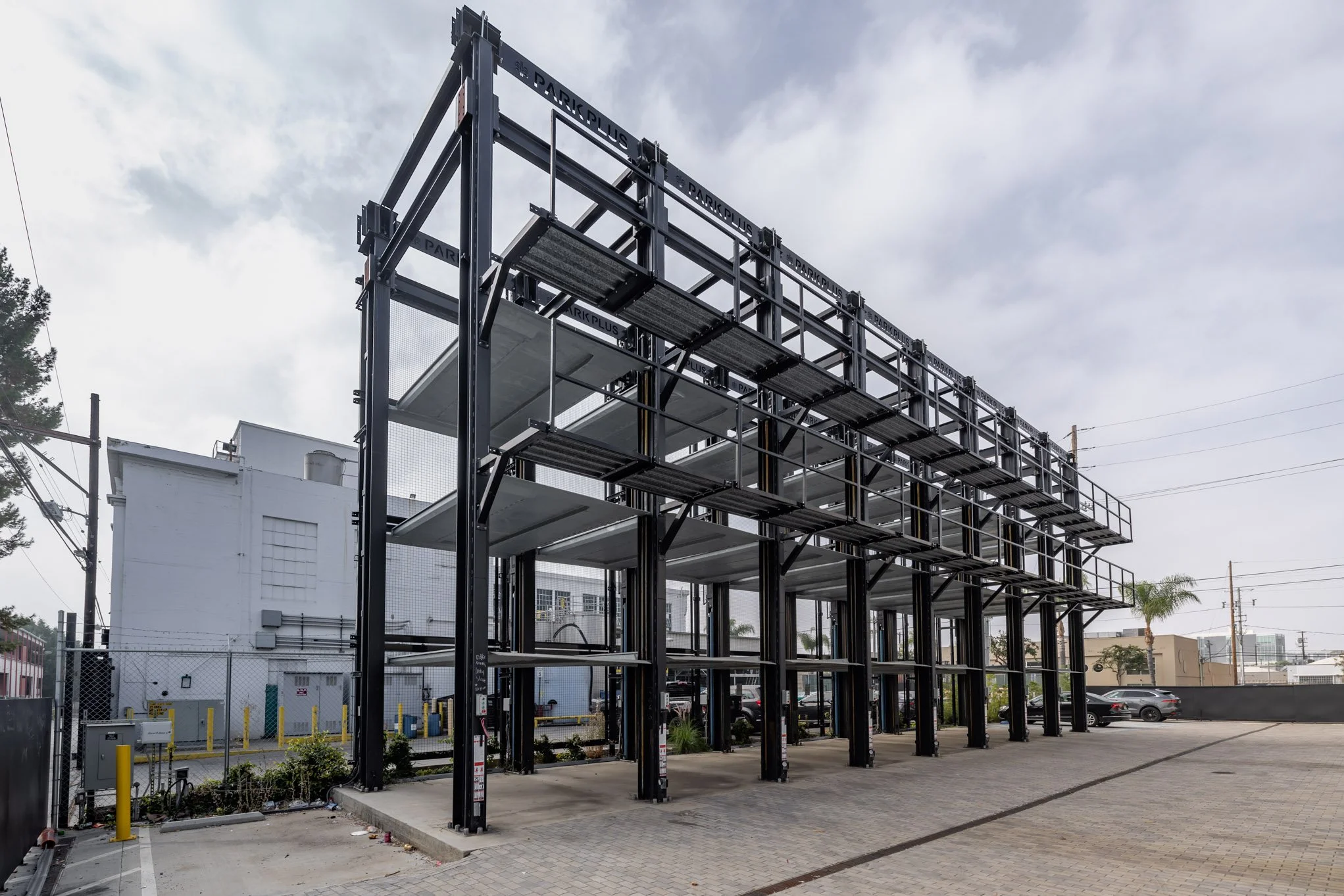 Empty multi-story parking structure with a black metal frame and concrete floors, in an urban area under a cloudy sky.