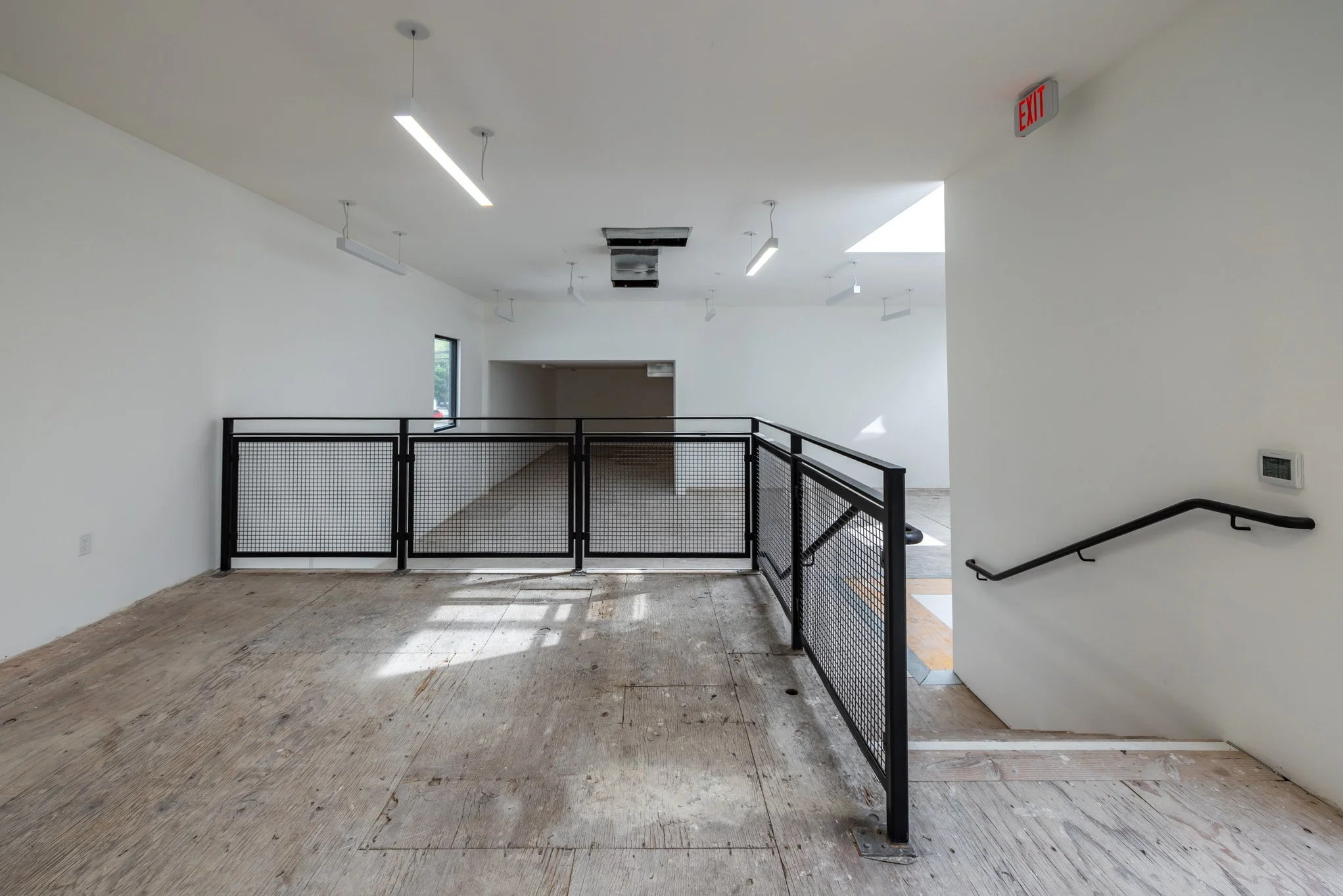 Empty interior space with white walls, a metal railing, and a wooden floor in-progress of installation.
