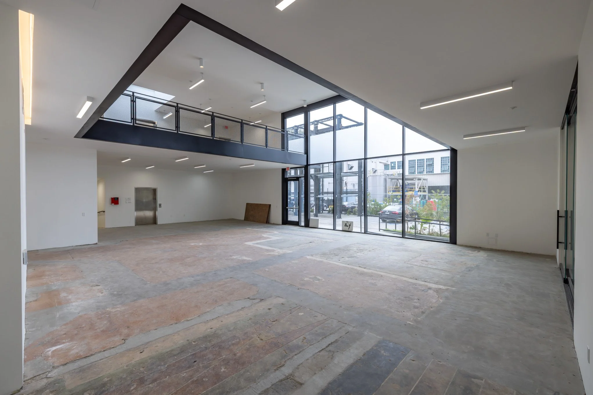 Empty commercial space with large glass windows, polished concrete floors, white walls, and a second-floor balcony with a black railing.