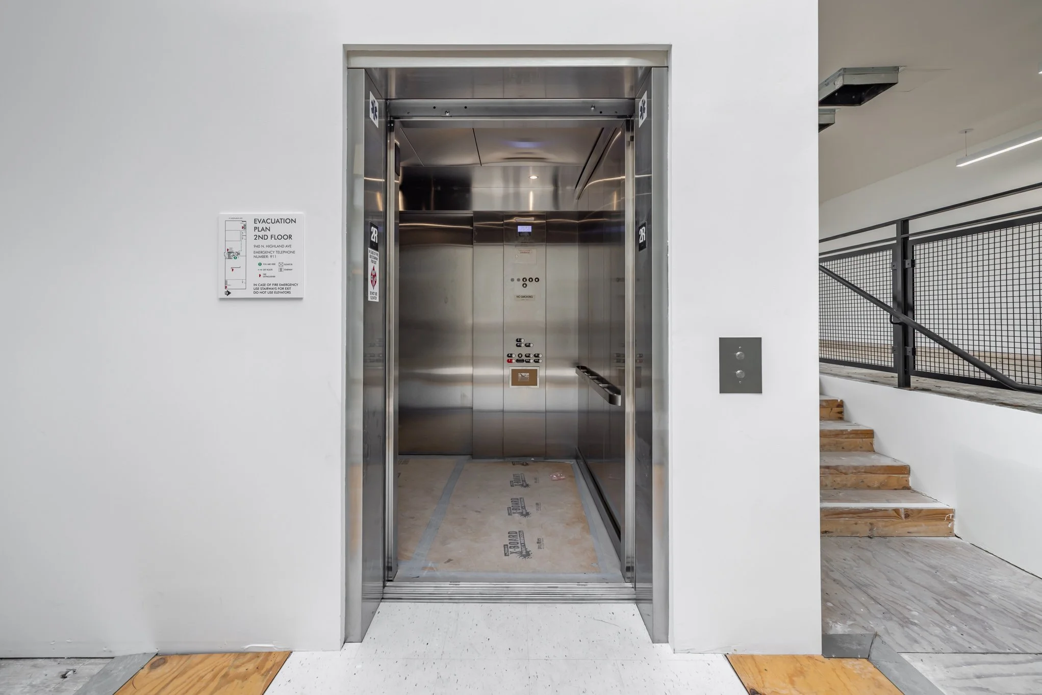 Interior of a modern elevator with stainless steel walls, control panel, and floor indicator, located in a building under construction or renovation.