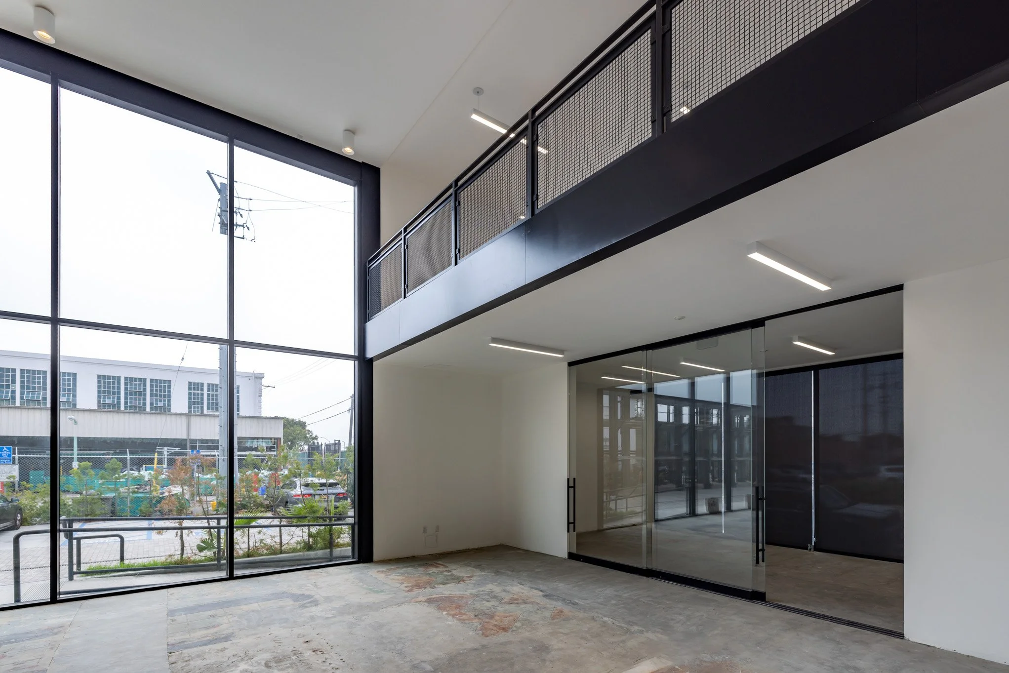 Empty commercial space with large floor-to-ceiling windows, glass entrance doors, and a second-floor balcony with black metal railing.