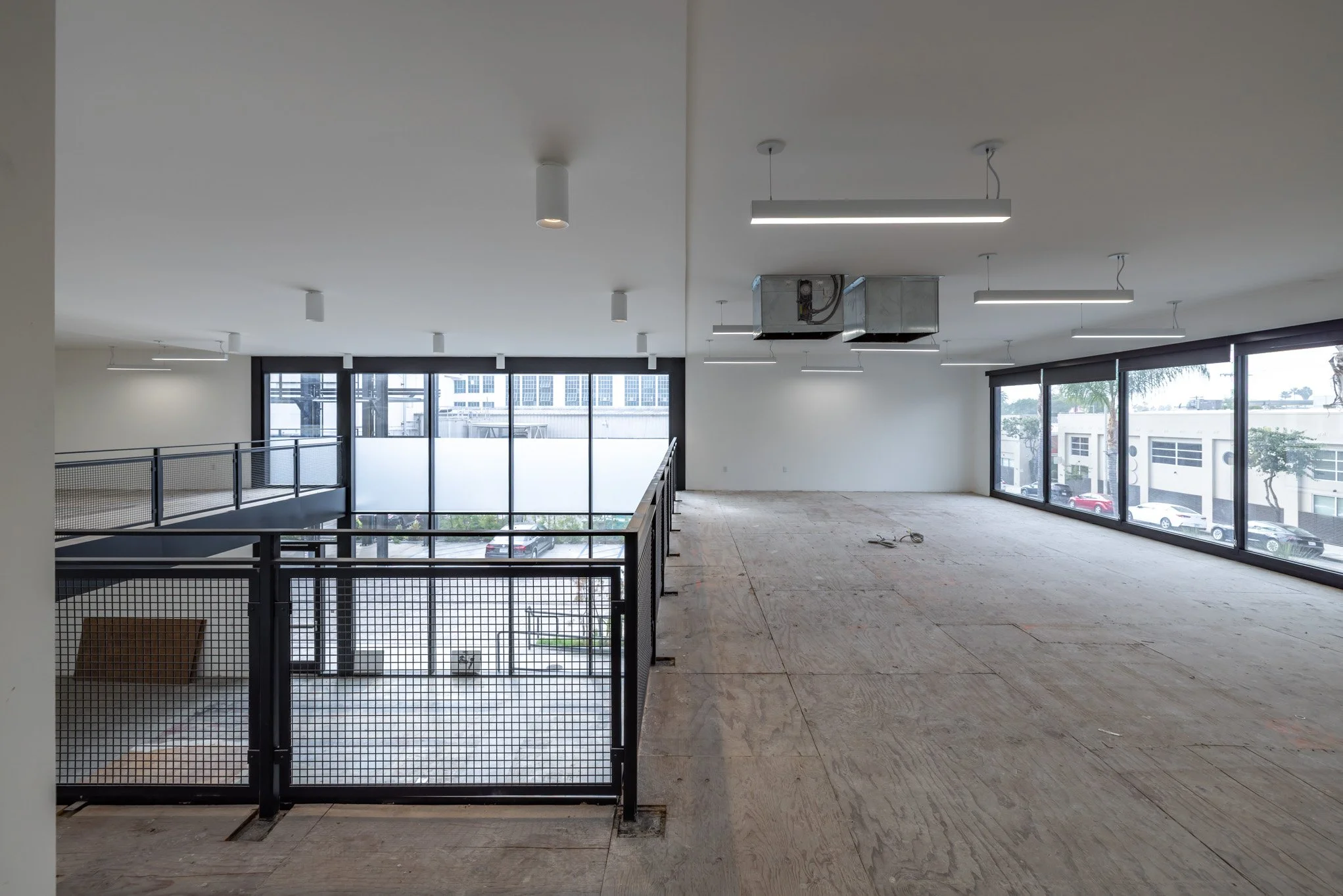 Empty commercial space with large windows, modern lighting, and exposed ductwork, partially under construction.