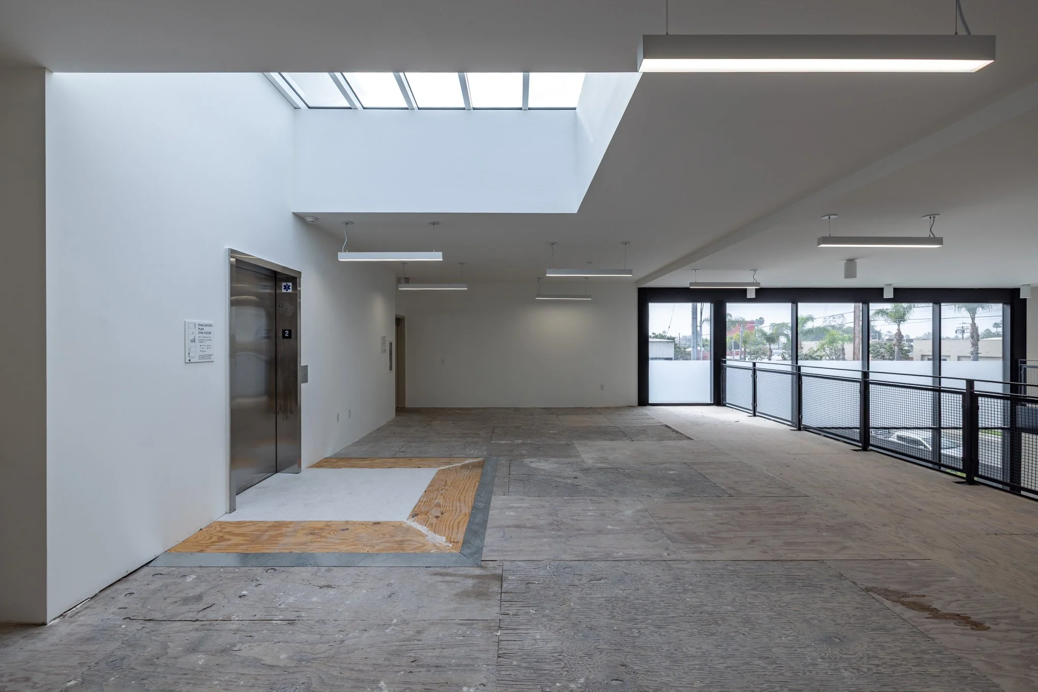 Empty indoor space with elevator, skylight, and large windows, under construction or renovation.