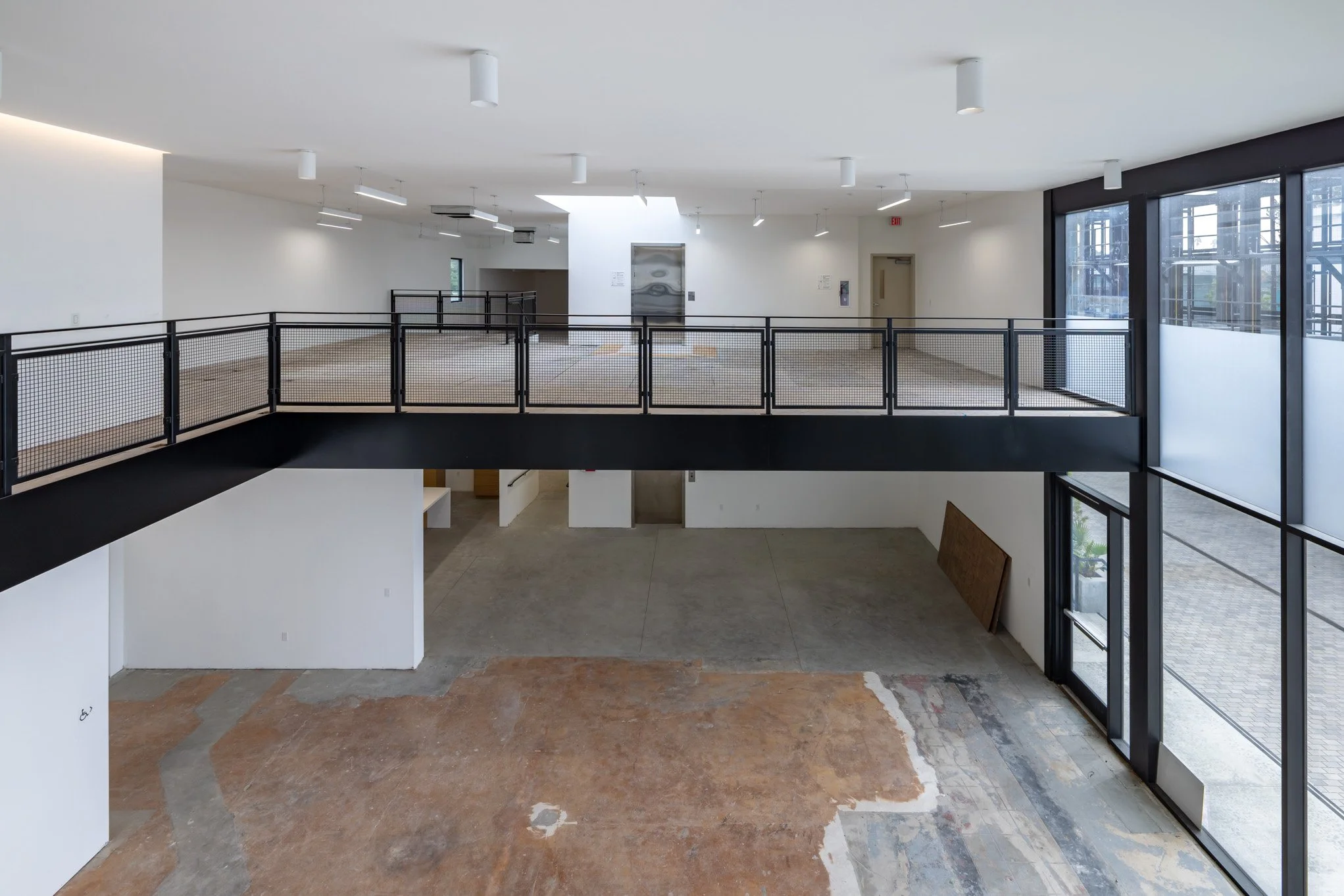 Empty multi-level interior space with large windows, black railing, and unfinished flooring.