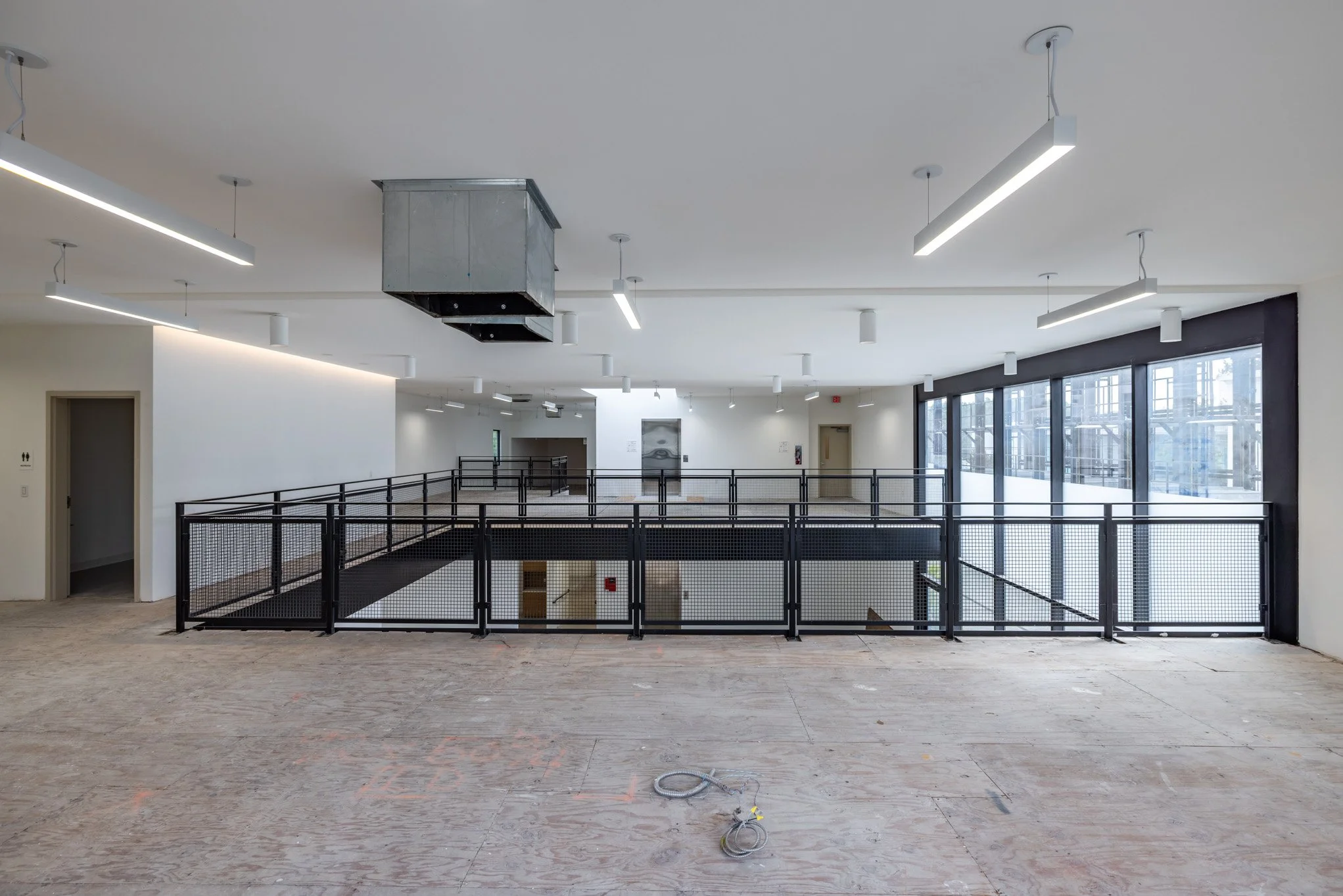 Interior of a modern building under construction with a large open space, black metal railing, and large windows letting in natural light.