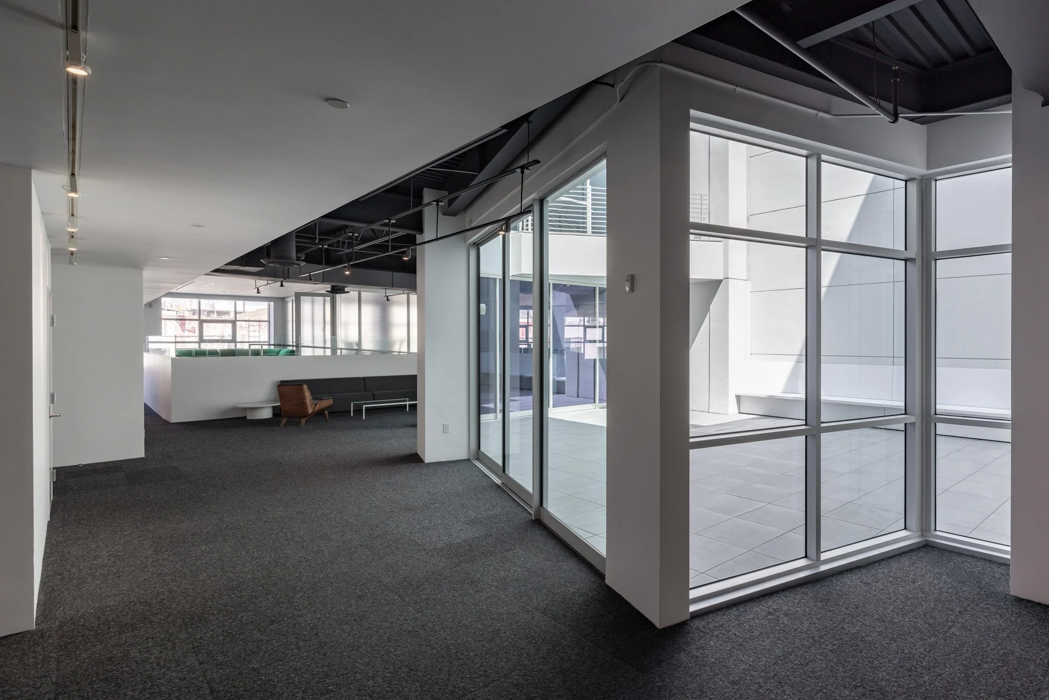 Empty modern office space with large glass windows, gray carpet, and minimal furniture.