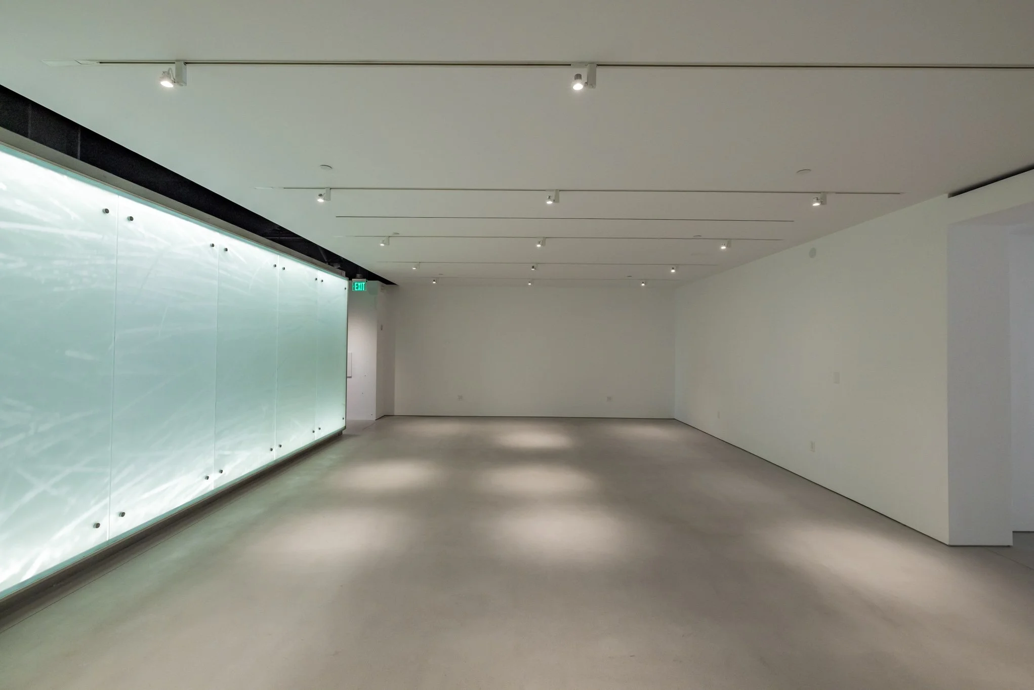 Empty modern art gallery with white walls, polished concrete floor, and a large backlit glass wall on the left side.