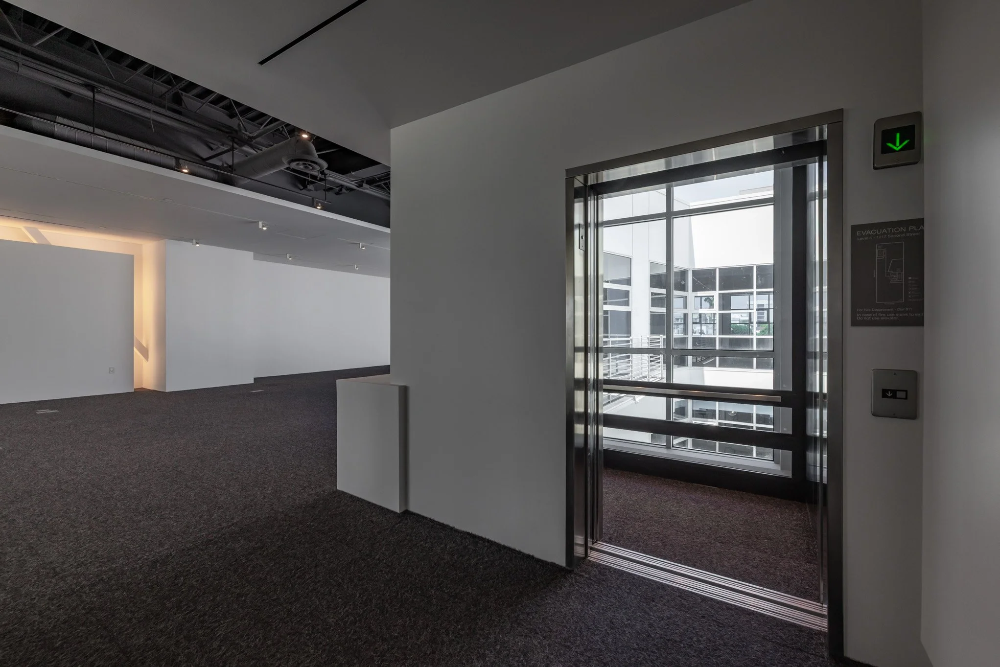 Empty modern office or commercial building interior with elevator doors open, showing a view of glass-walled corridors outside.