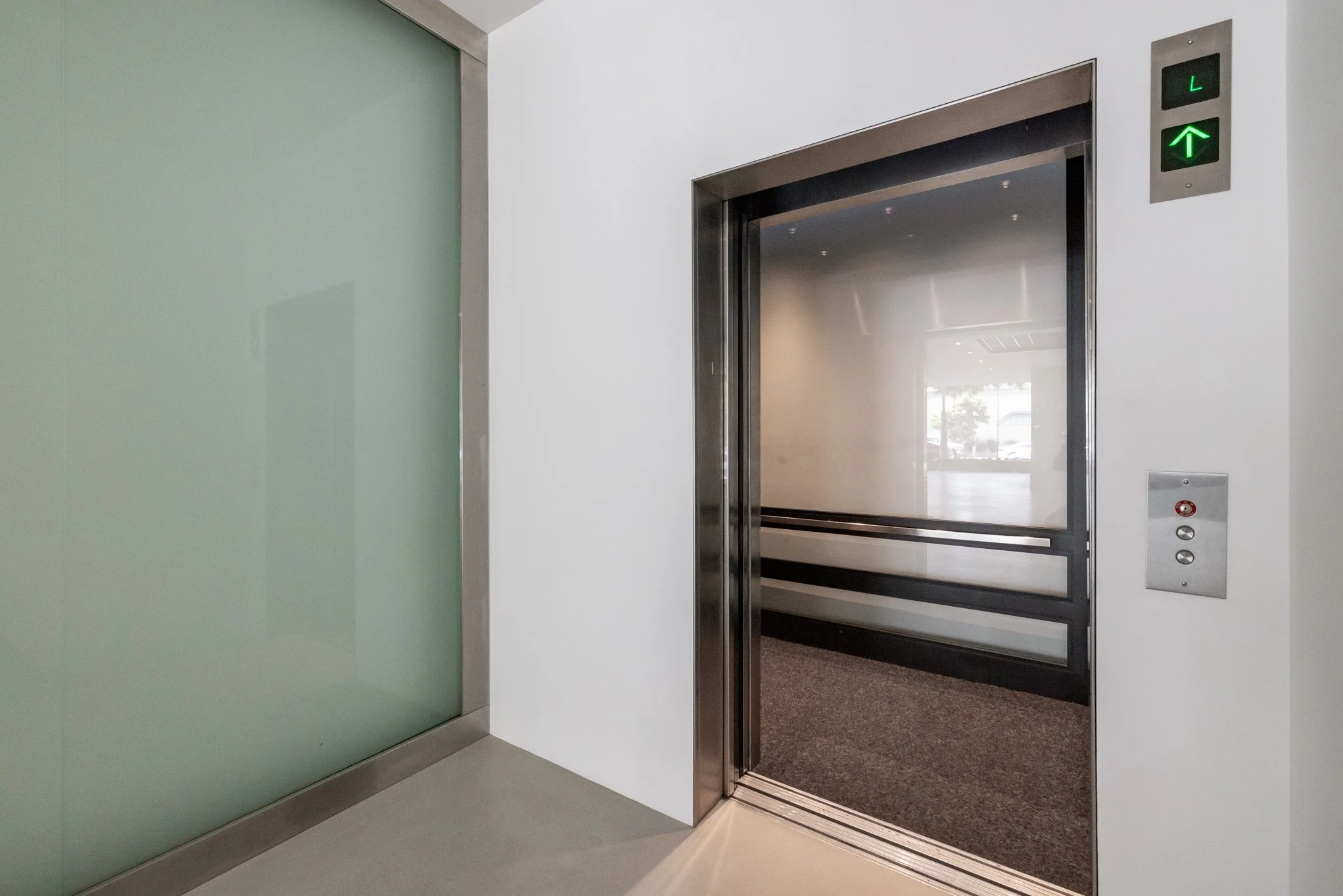 Elevator with open door in a modern building hallway, showing interior and call buttons.