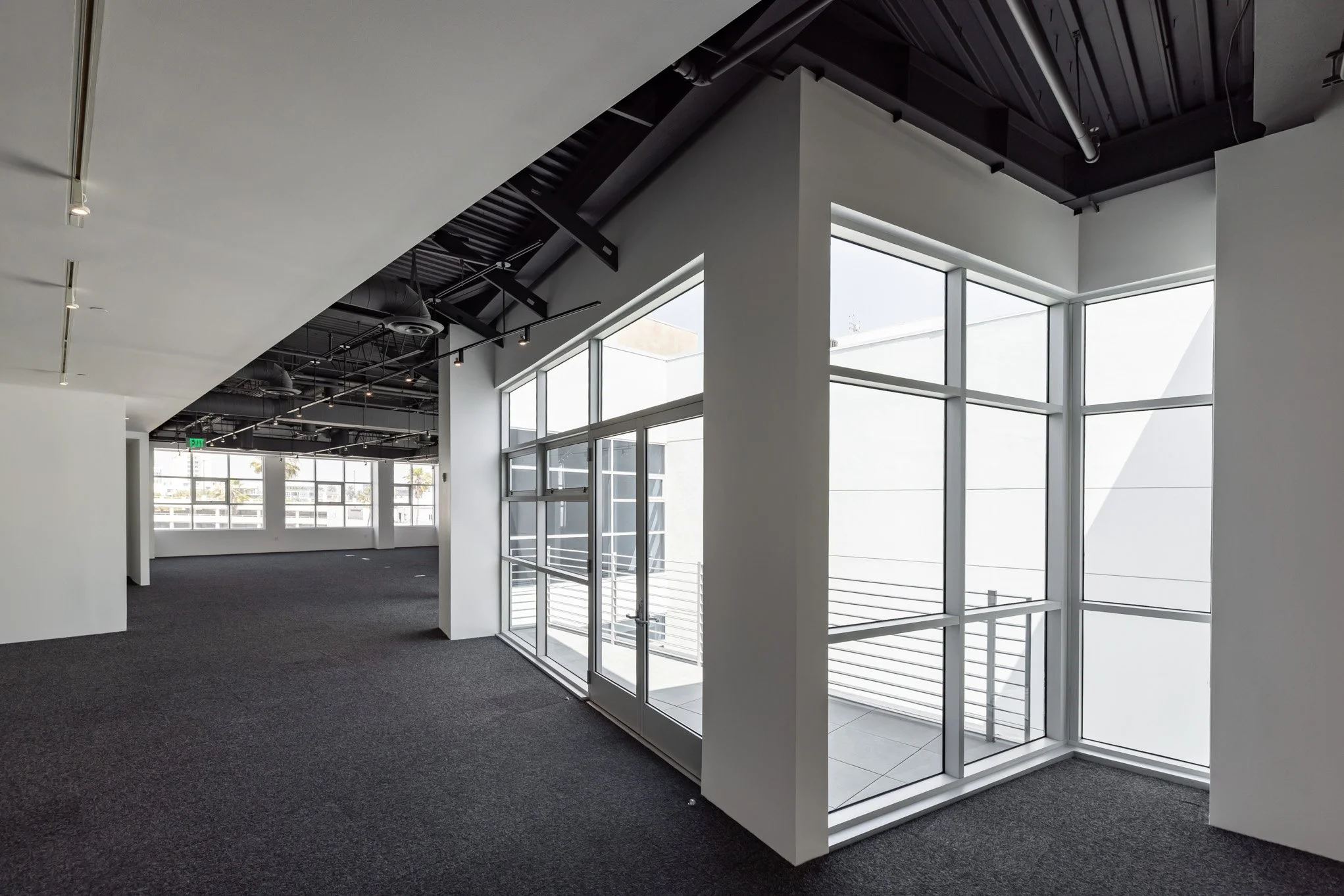 Empty modern office space with large glass windows, black ceiling, and gray carpeted floor.