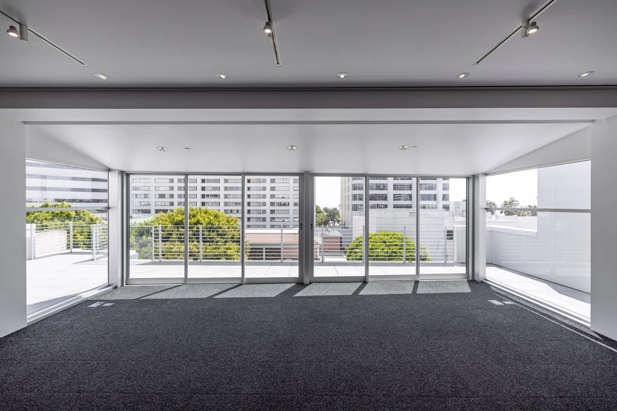 Empty modern room with sliding glass doors opening to a balcony, view of trees and tall buildings outside.