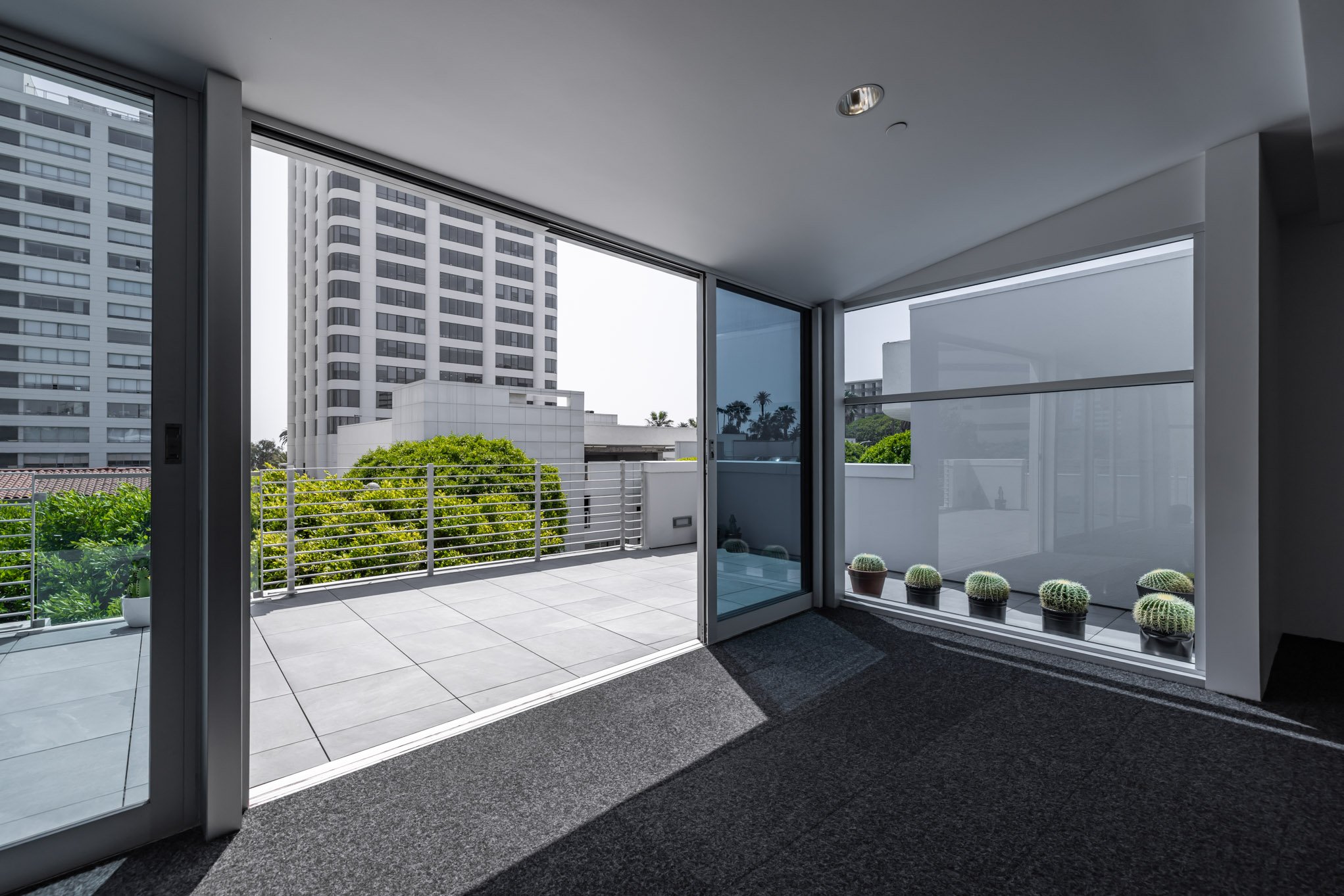 Indoor room with large sliding glass door opening to a balcony with potted cacti and cityscape view