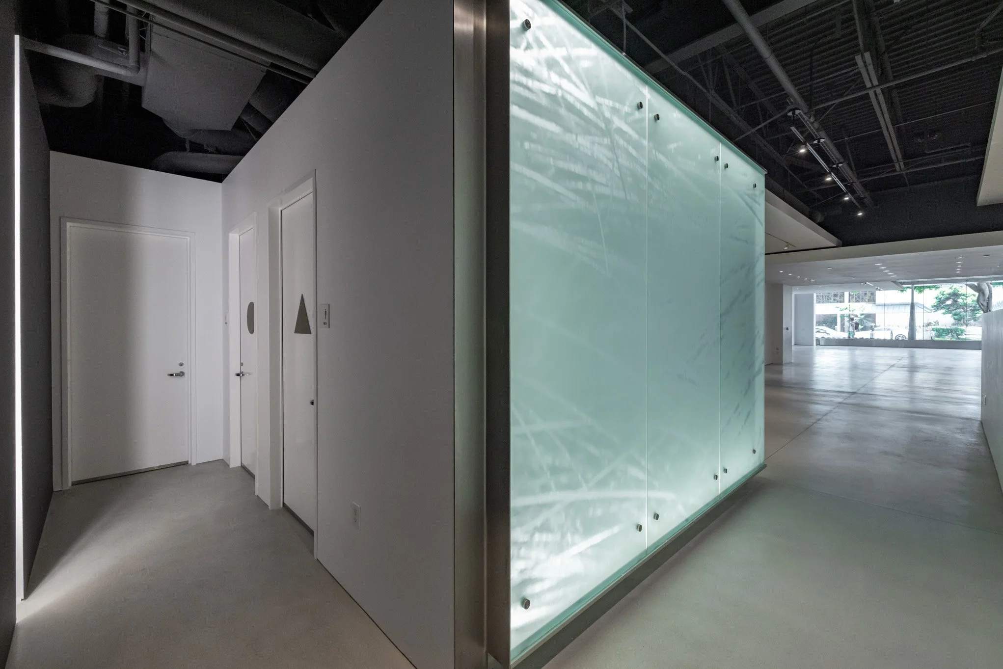 Interior space with white walls, white doors, and a frosted glass wall, in a modern building with an open area and large windows.