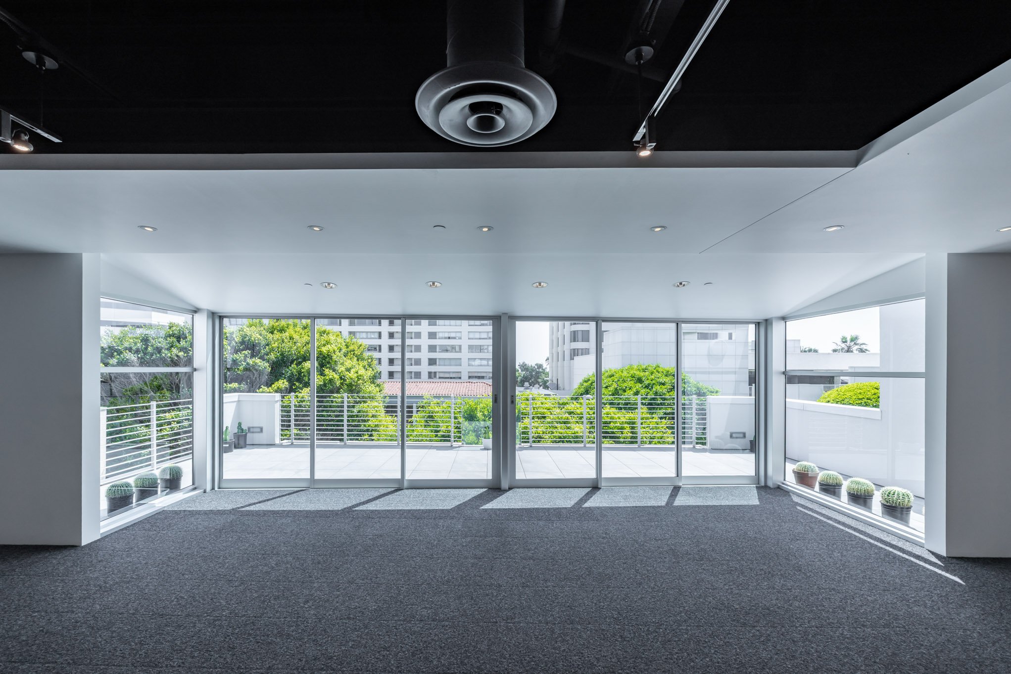 Empty modern room with large sliding glass doors leading to a balcony with potted plants and city view.