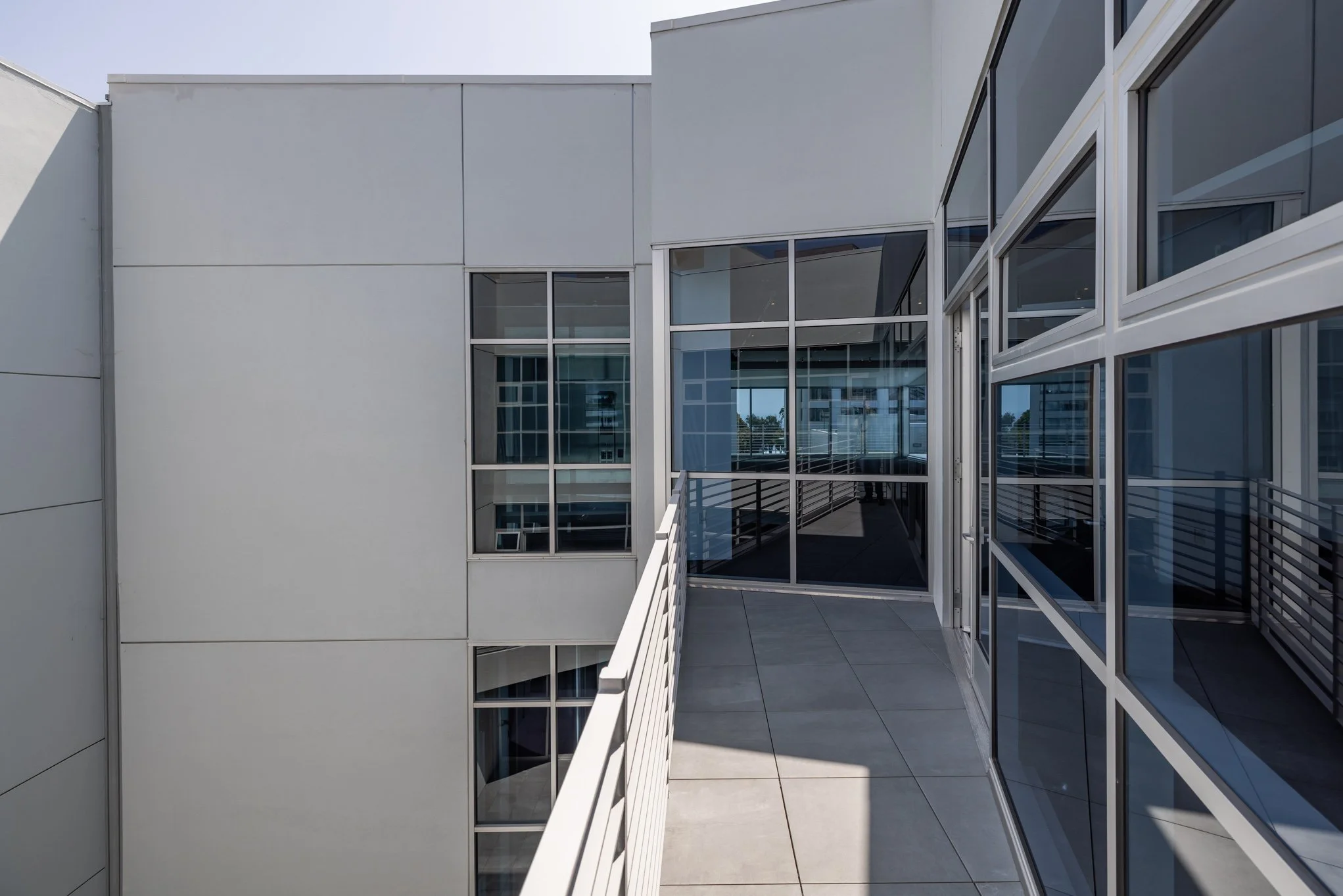 View from a balcony of a modern building with glass windows and metal railing, showing the exterior of the building with white walls and multiple windows.