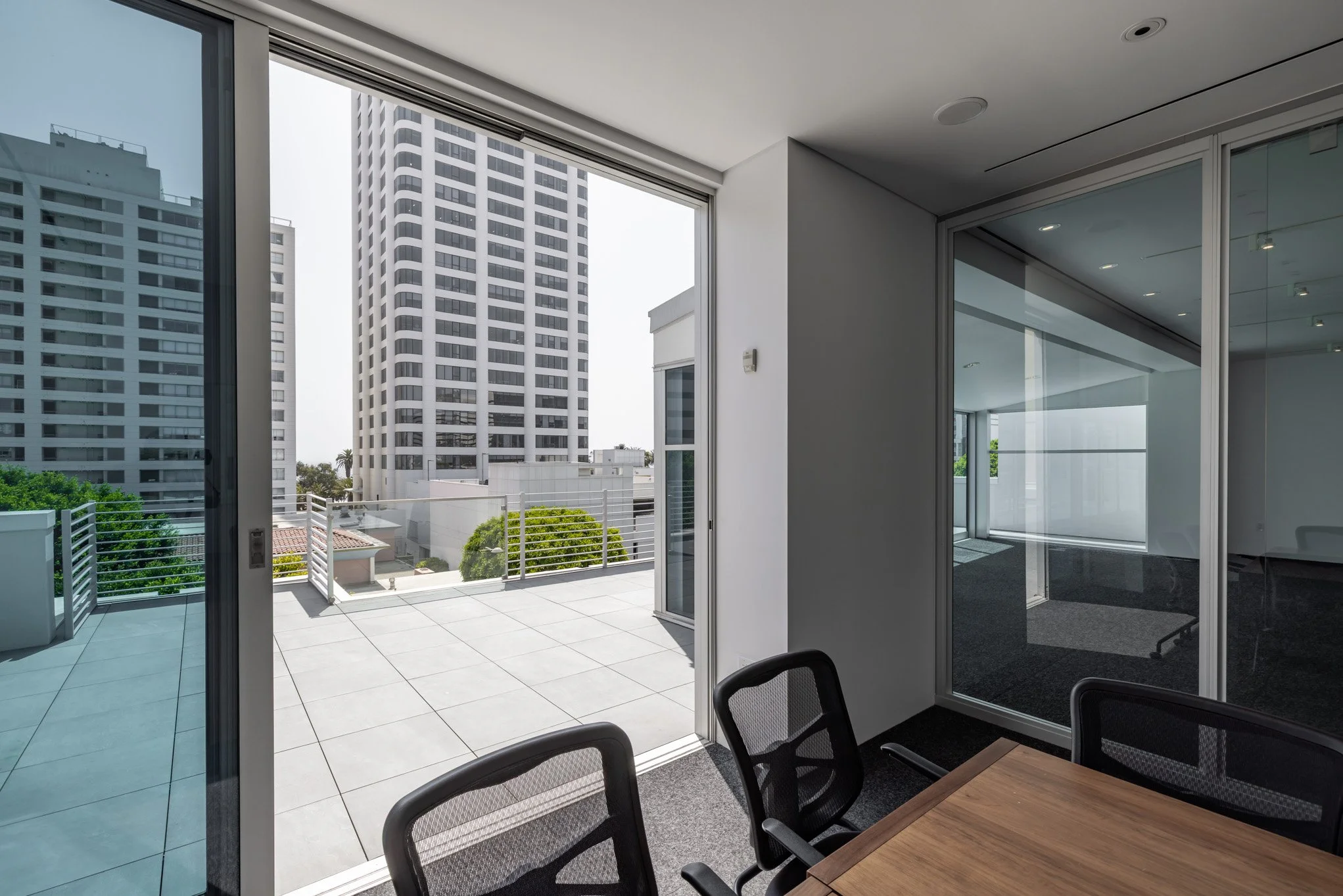 Office room with large glass sliding door opening to balcony with cityscape view of tall buildings