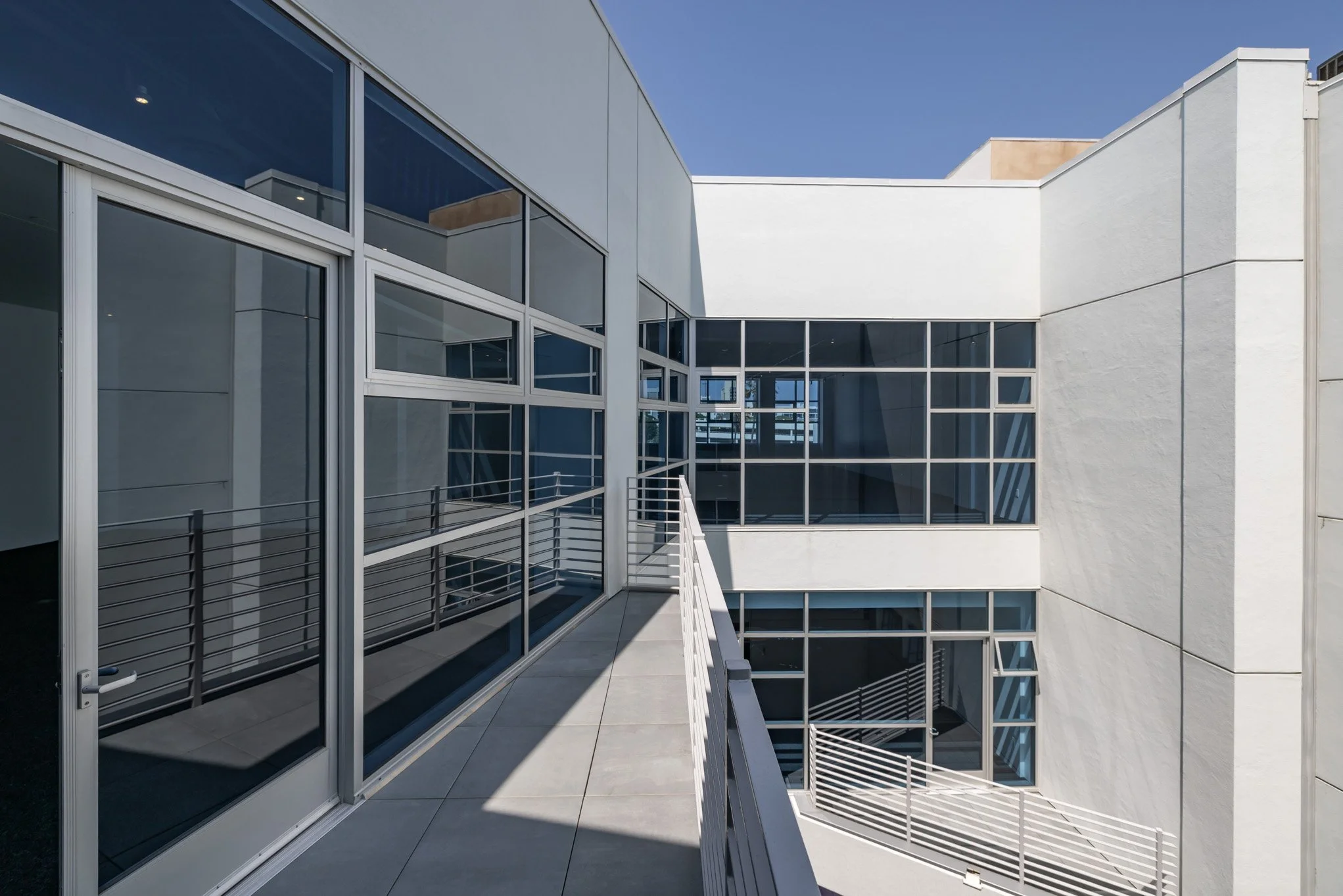 Modern building exterior with large glass windows and metal railings on a sunny day.