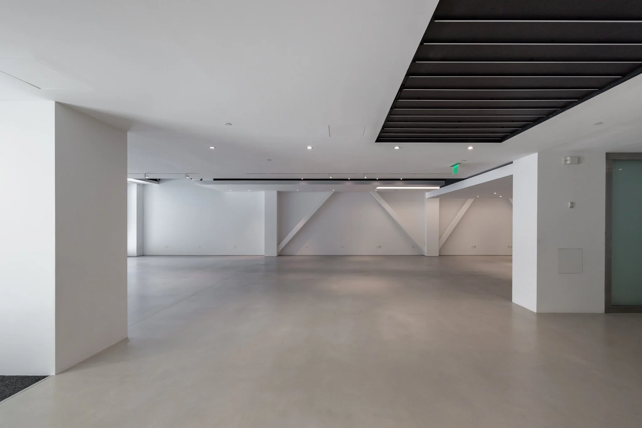 Empty modern interior with white walls, concrete floor, and ceiling with black accents and small recessed lighting.