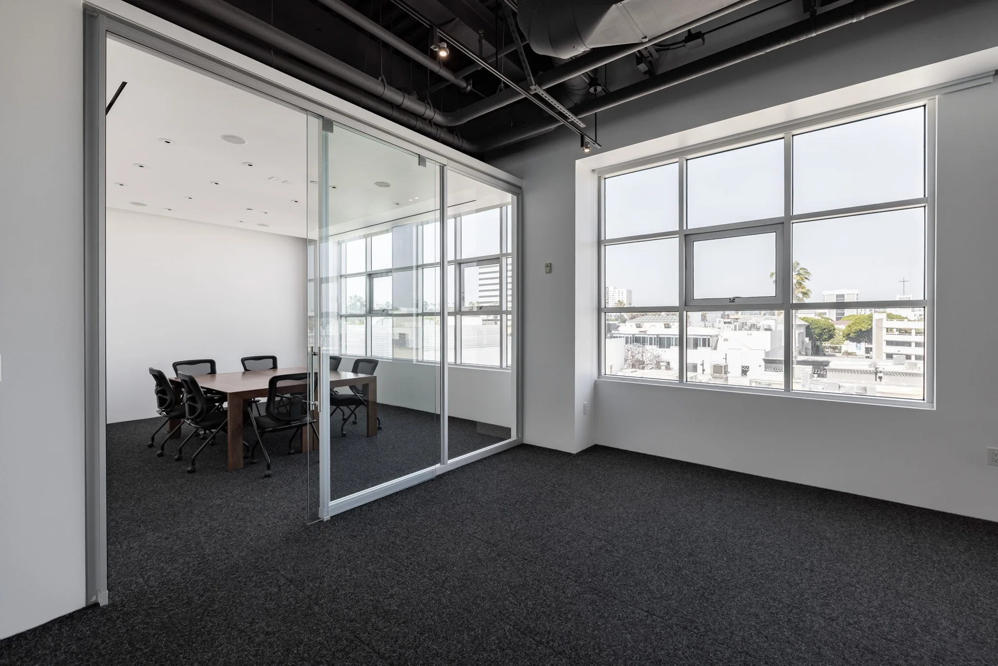 Empty modern conference room with large windows, black carpet, and a wooden table surrounded by black chairs, and a glass-walled meeting space.