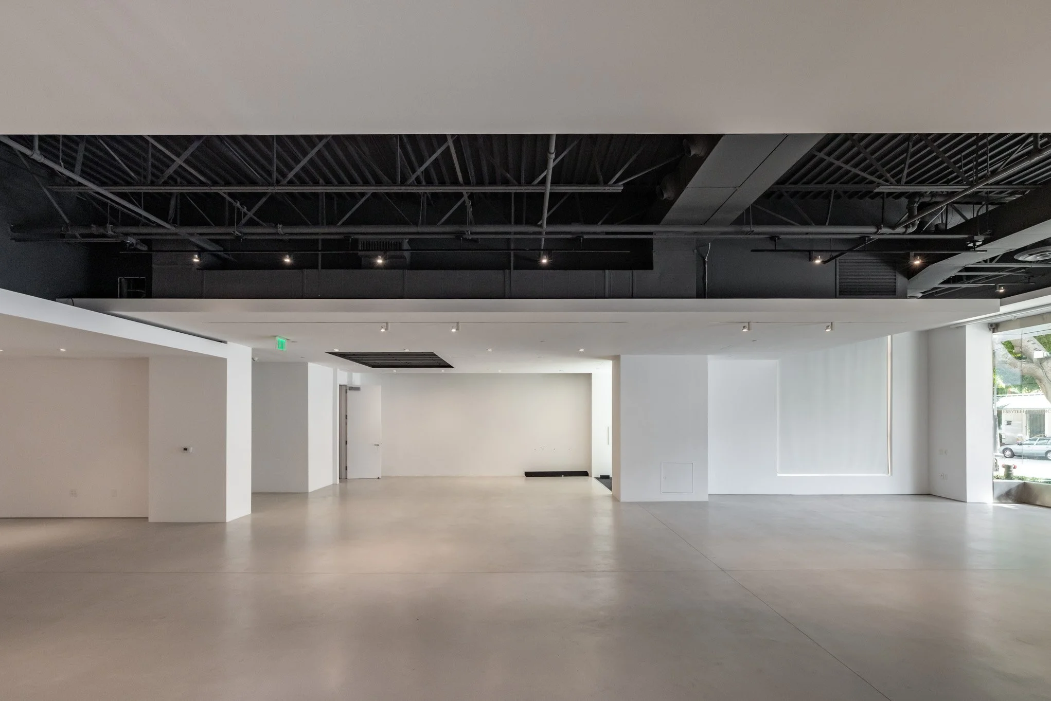 Empty, modern interior space with white walls, concrete floor, and exposed black ceiling with ductwork and lighting.