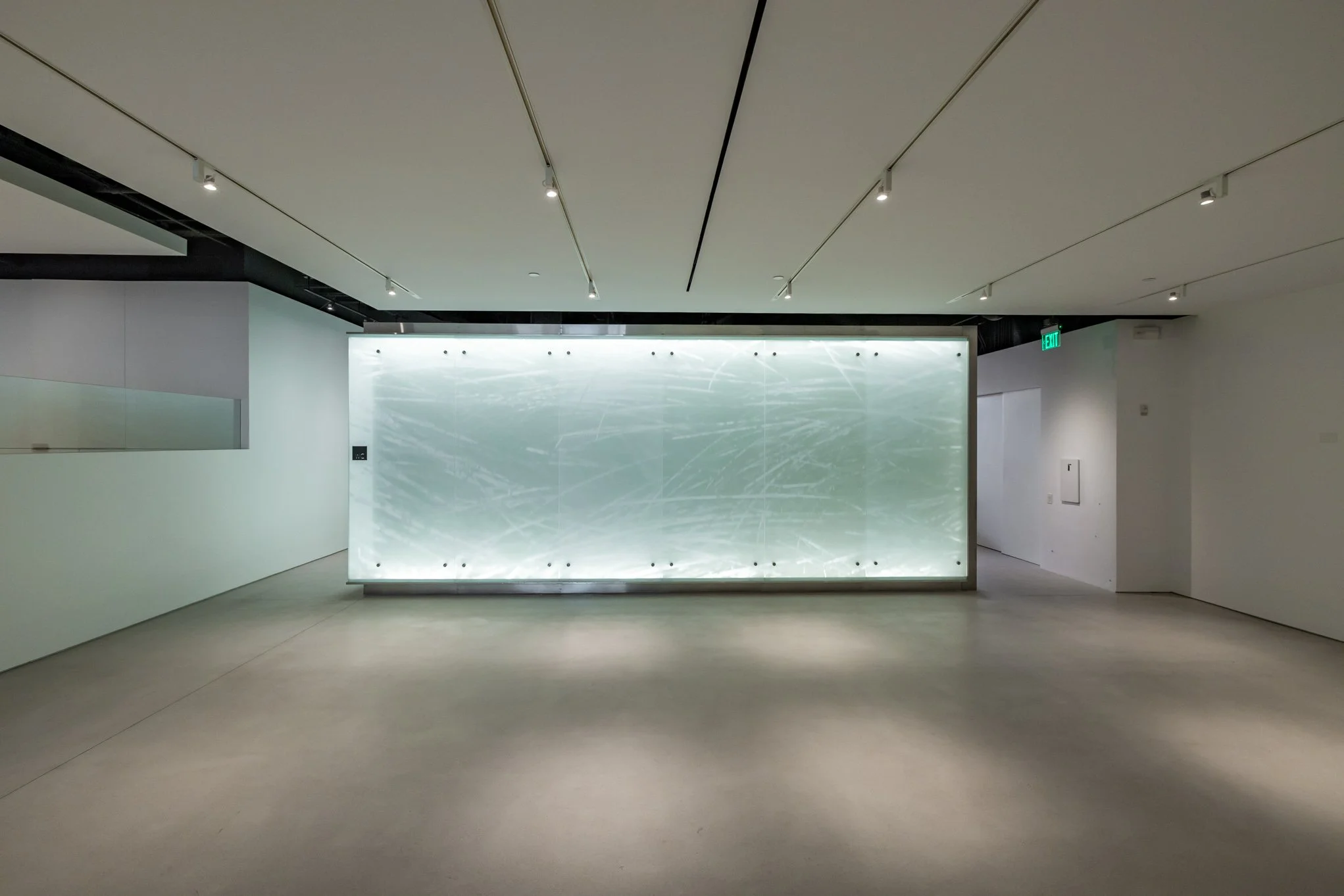 Modern art installation of a backlit panel with abstract white lines and patterns in a minimalist gallery space.